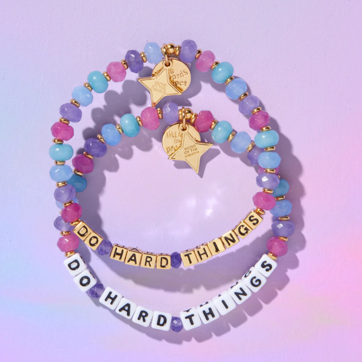 Do Hard Things September Word of the Month bracelets in both white letter bead and gold letter bead colorways, stacked flat on a lilac background