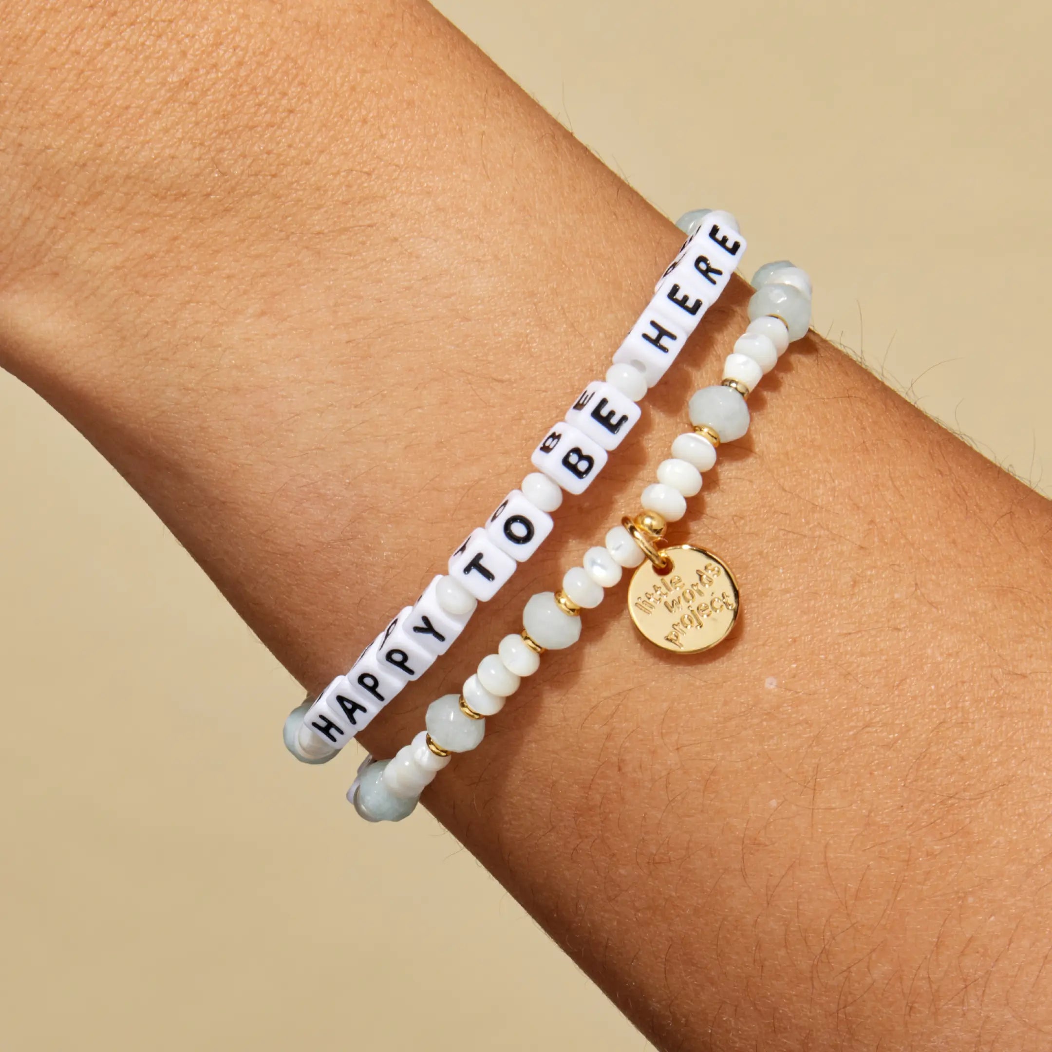 Bracelet with 'Happy to be here' message on a wrist against a beige background