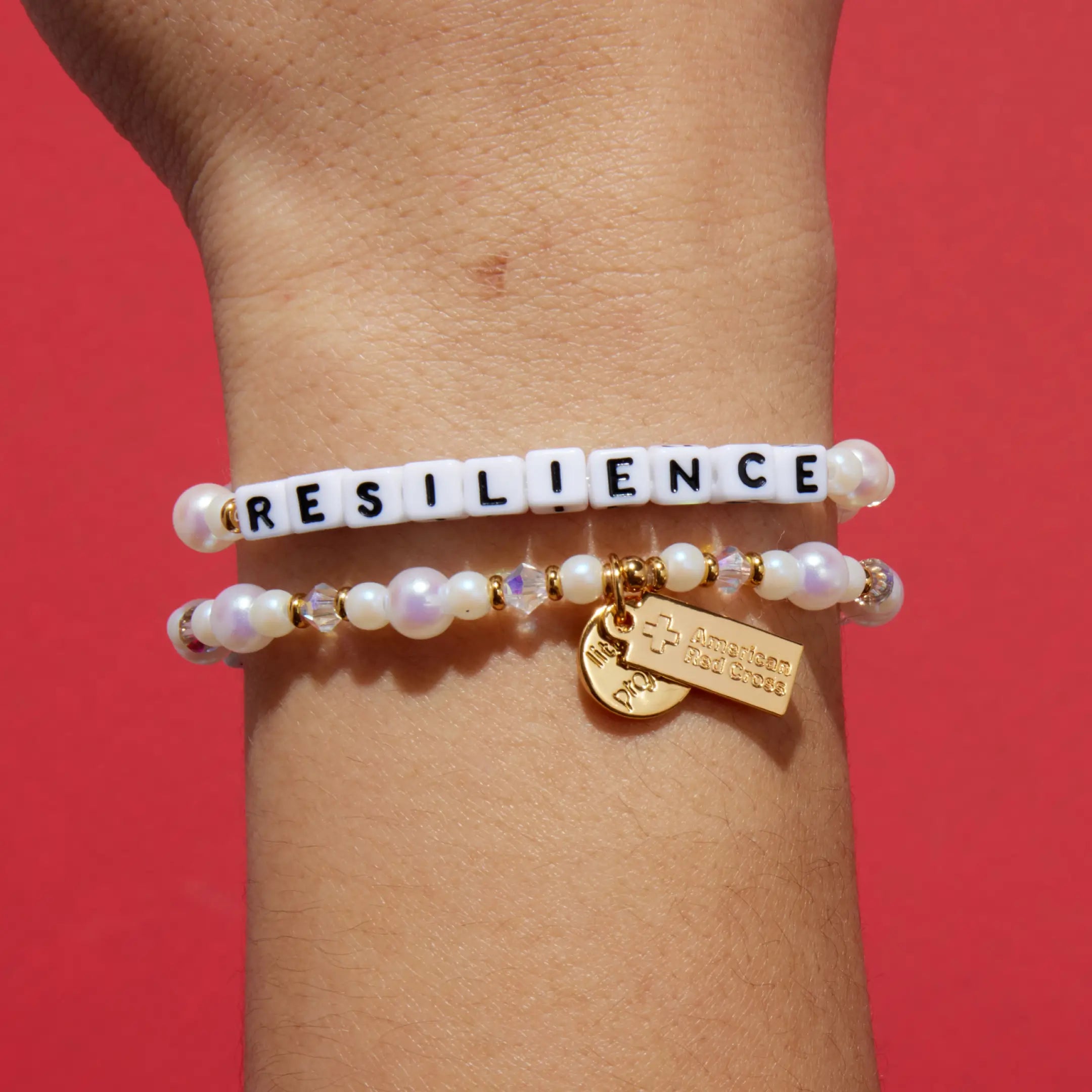 Bracelet with 'RESILIENCE' beads on a wrist against a red background