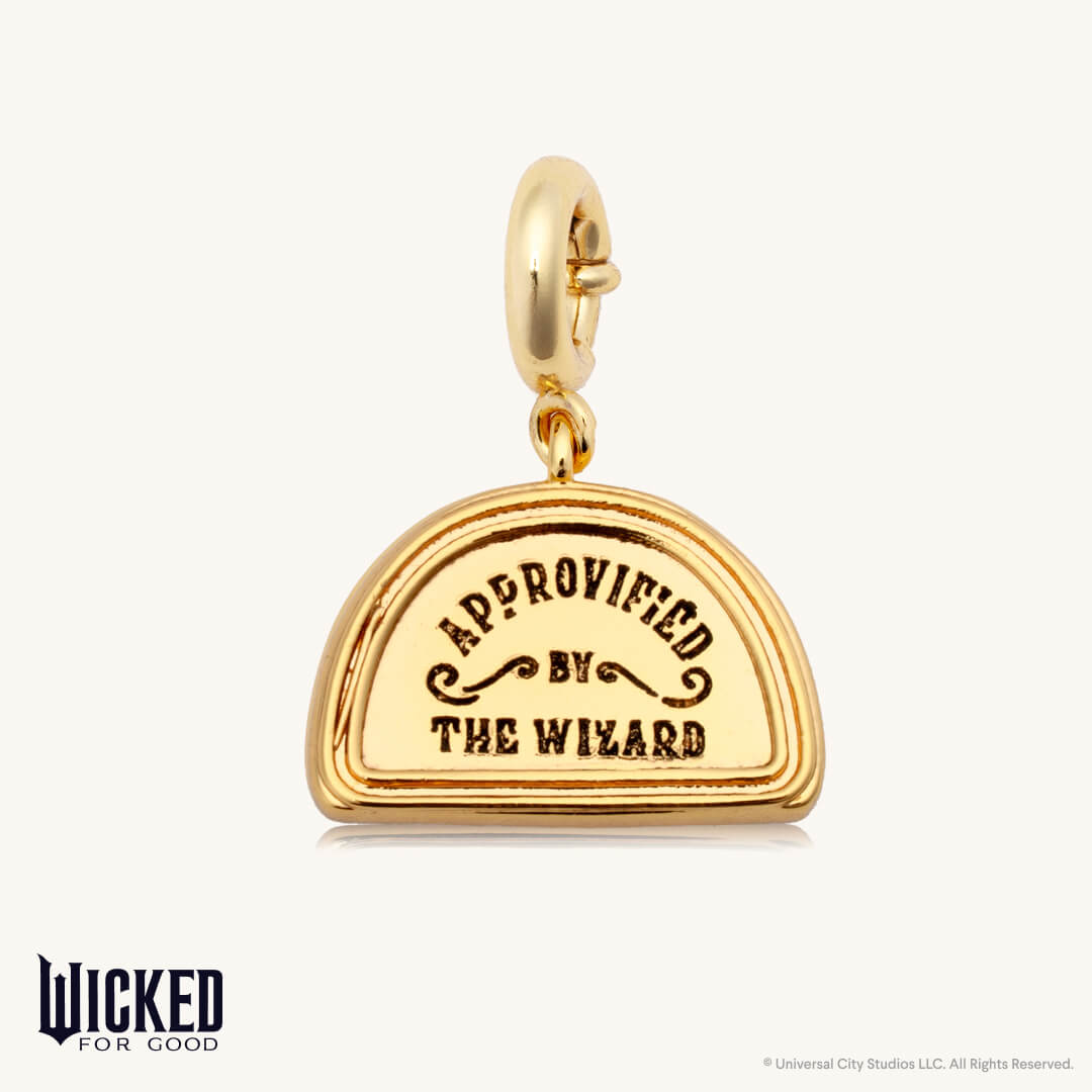 Gold charm with 'Approved by The Wizard' text on a white background, featuring the Wicked For Good logo.