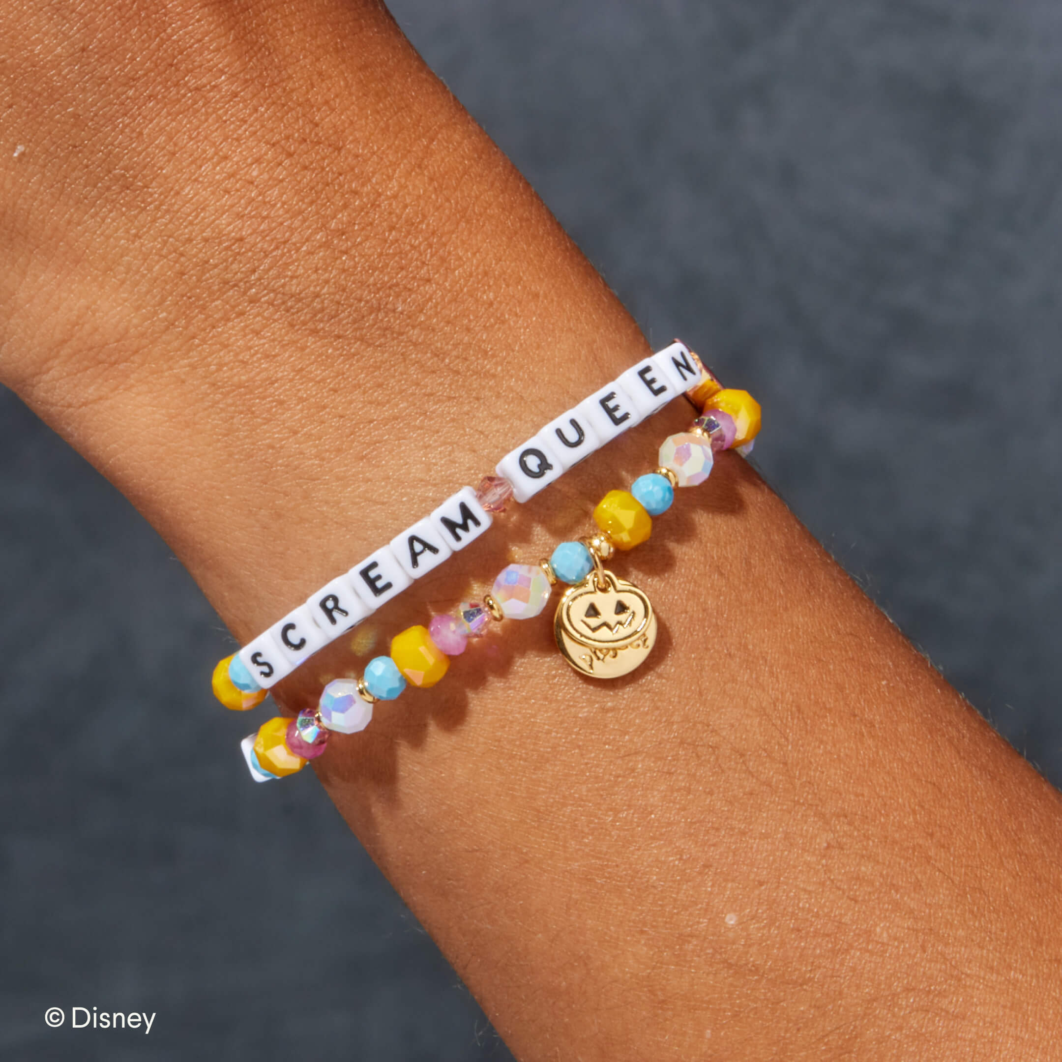 Colorful beaded bracelet with 'SCREAM QUEEN' text and pumpkin charm on wrist against a dark background.