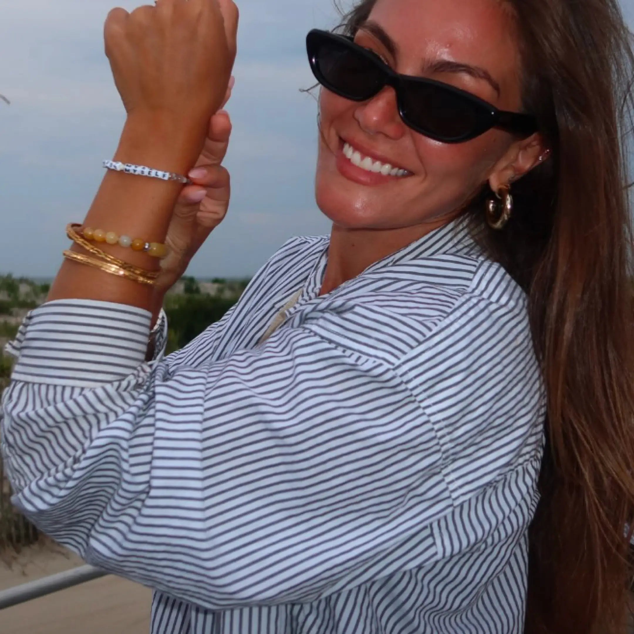 Model wearing the I Trust Myself Tori Deal Kindfluencer bracelet on her wrist outdoors, stacked with gold bangles and a yellow beaded bracelet