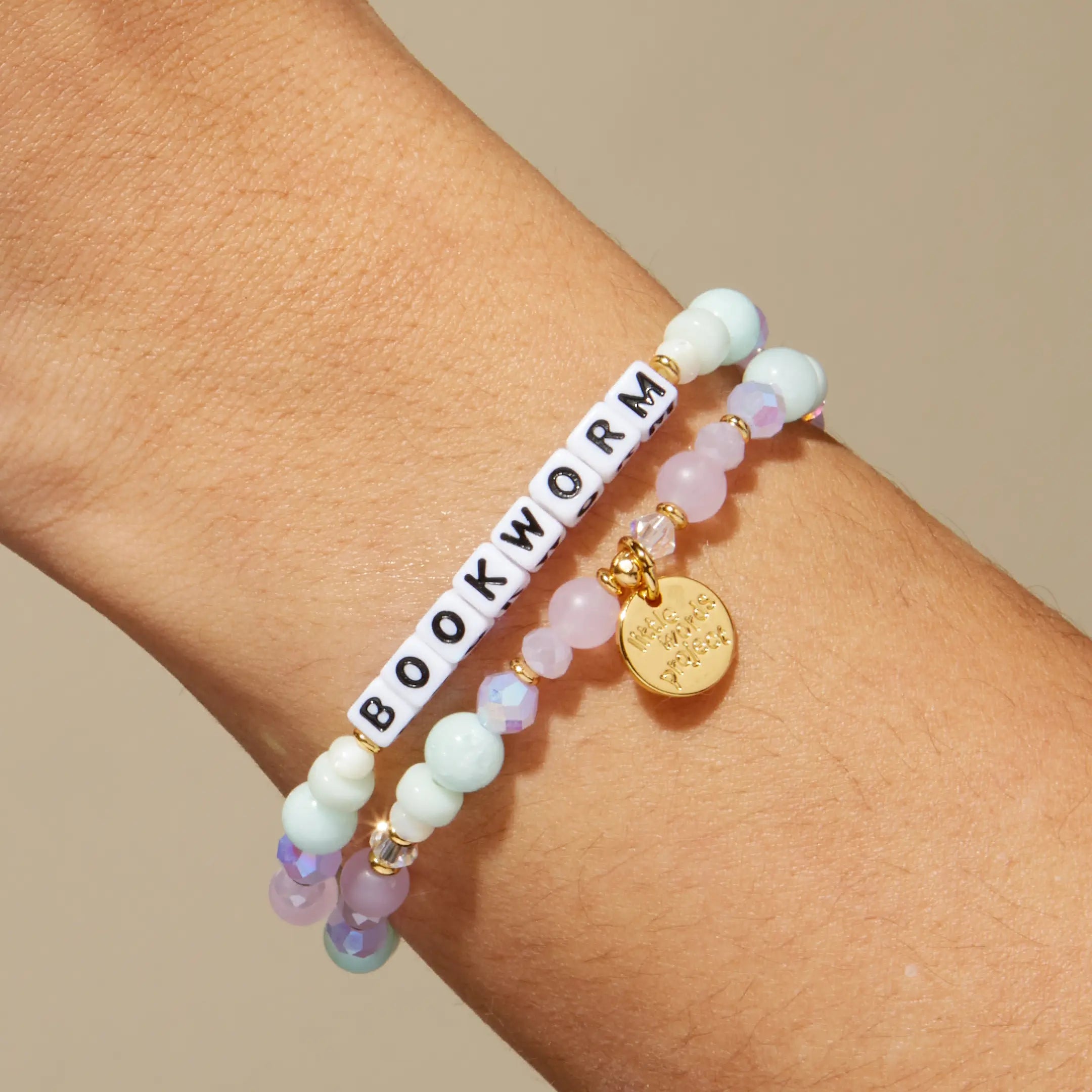 Bracelet with 'BOOKWORM' beads on a wrist against a beige background