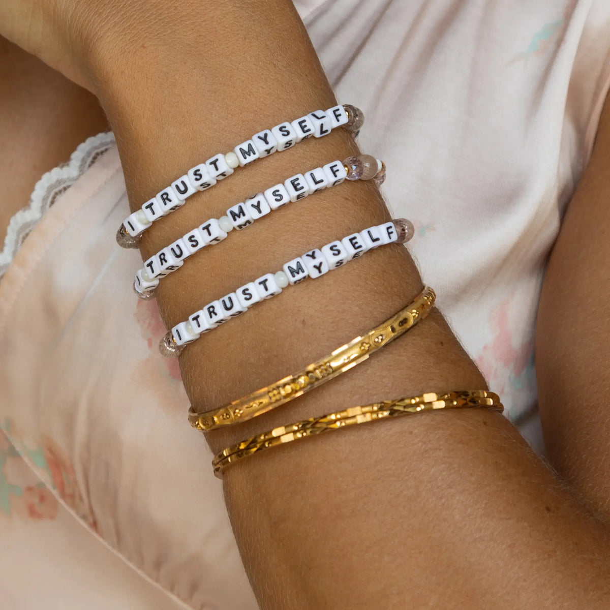 I Trust Myself Tori Deal Kindfluencer bracelets stacked three deep with gold bangles on model's wrist, white letter beads and clear crystals