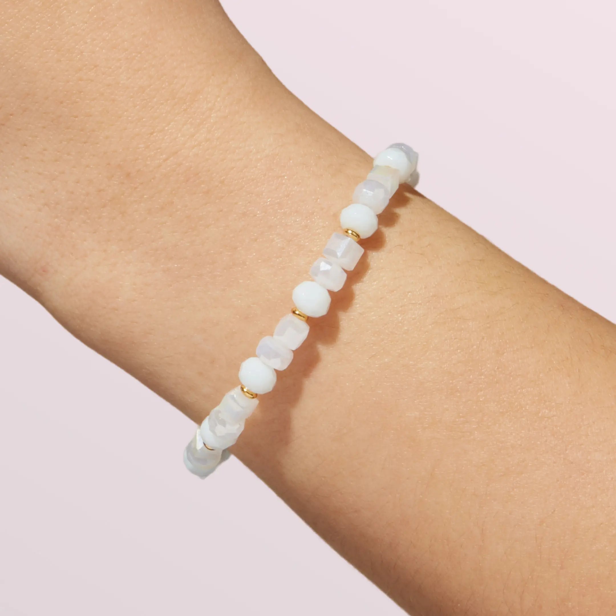White beaded bracelet on a wrist with a light pink background