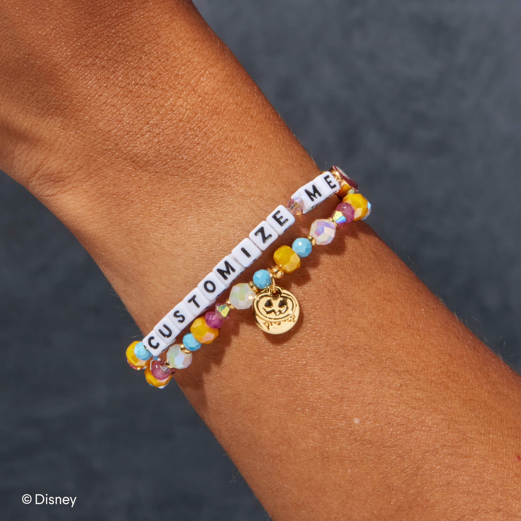 Bracelet with colorful beads and a gold charm on a wrist, against a dark background.
