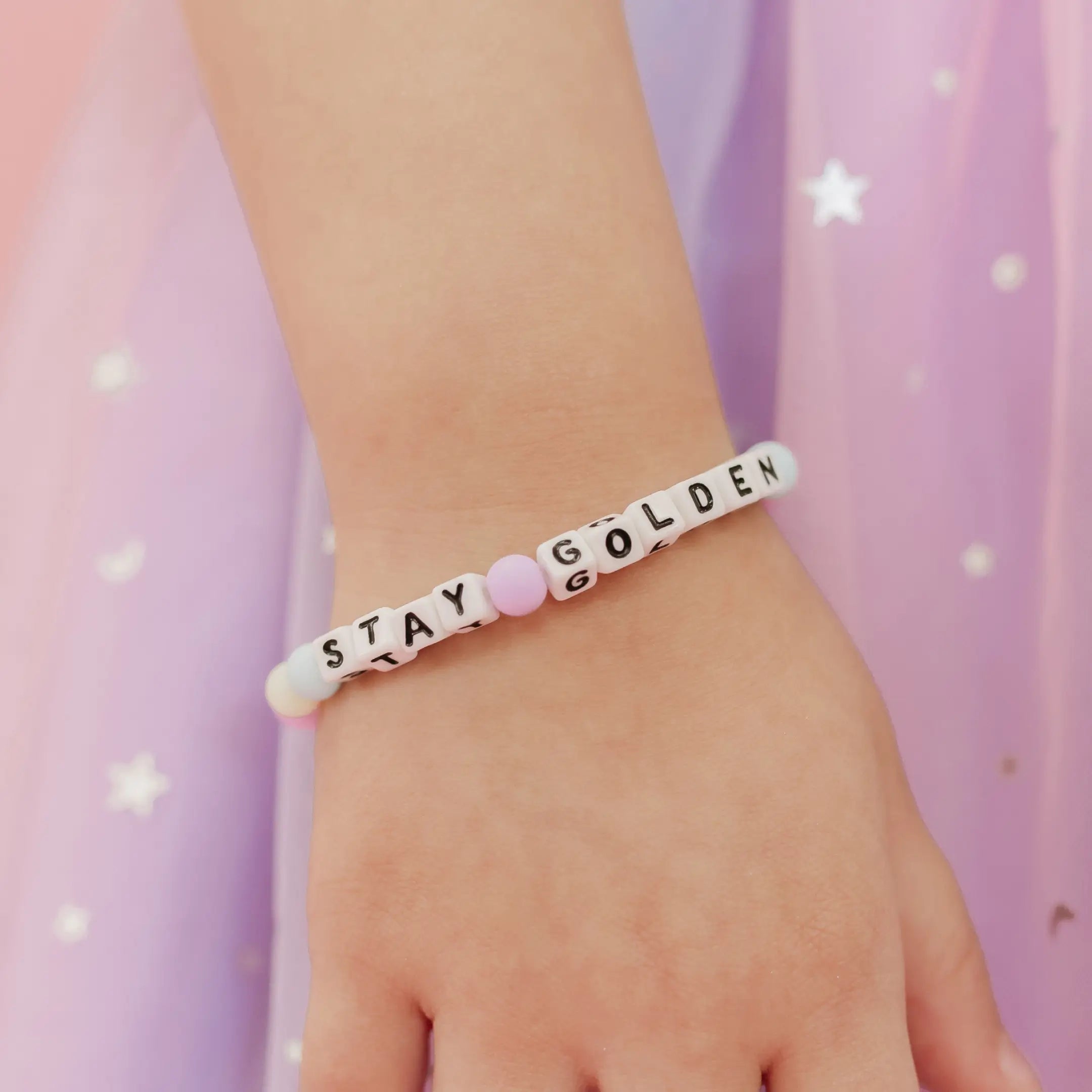 Stay Golden Kids Rylee Ta bracelet with white letter beads worn on a child's wrist next to a purple star tulle skirt