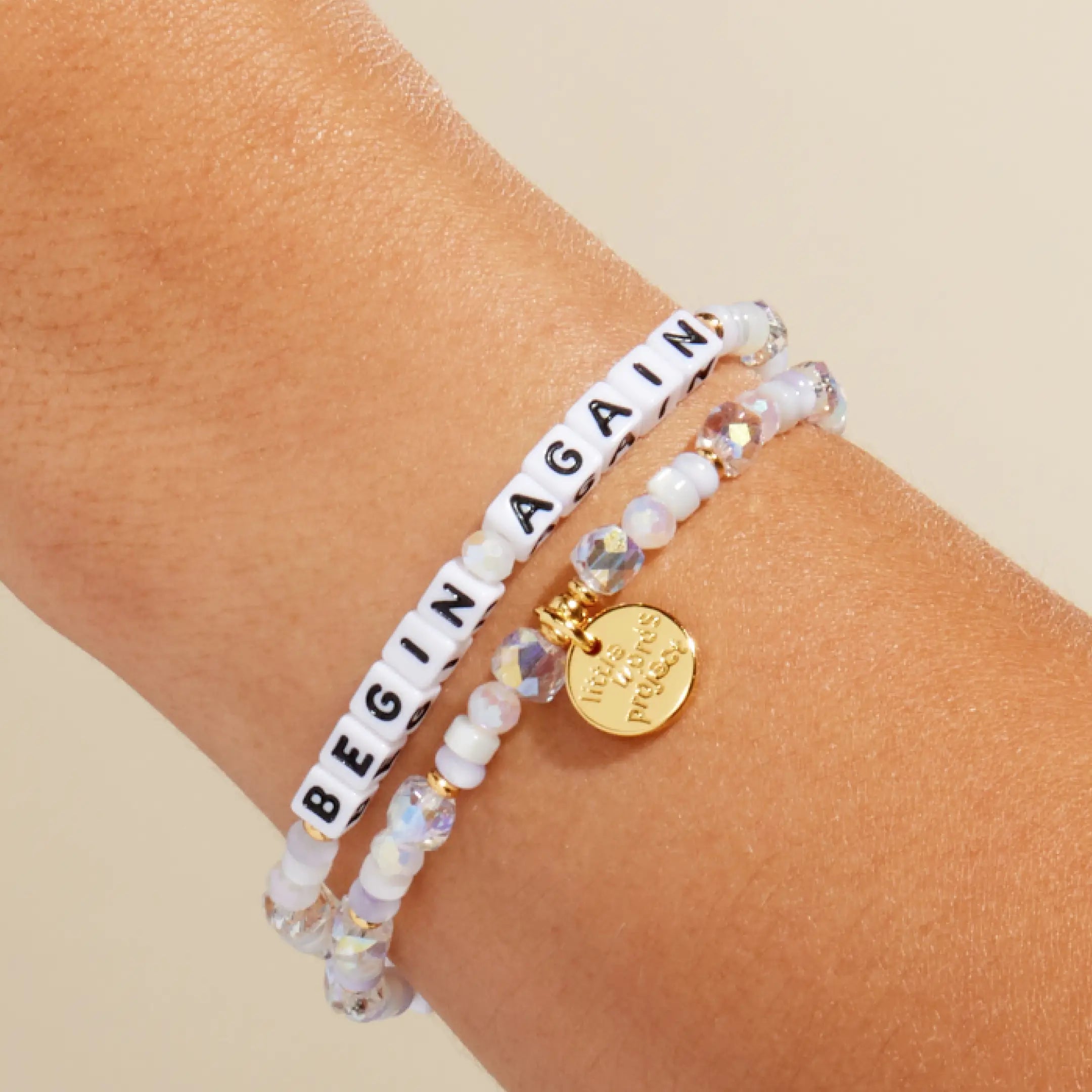Begin Again — on-model wrist shot of beaded word bracelet stacked with other bracelets in pastel and white beads