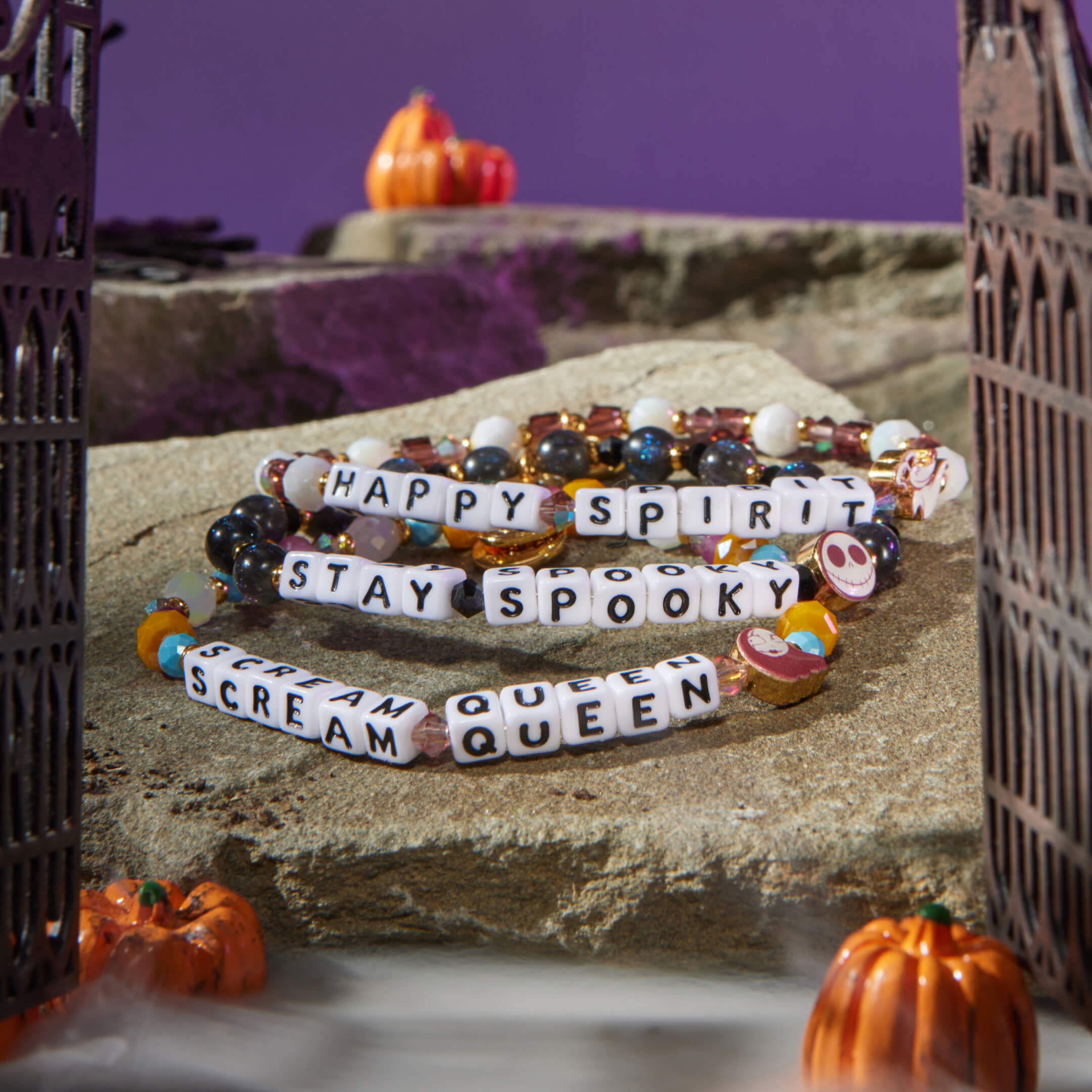 Halloween-themed bracelets with text on a stone surface with pumpkins in the background