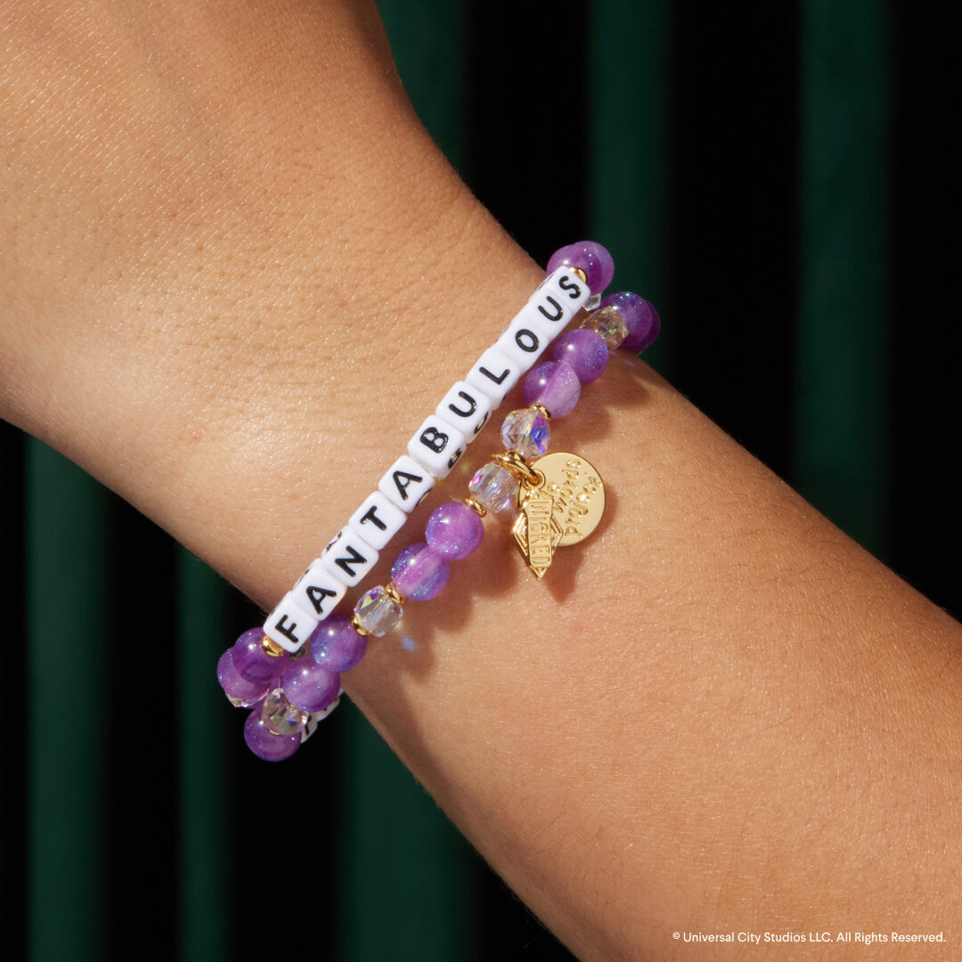 Bracelet with purple beads and gold charm on a wrist against a dark background