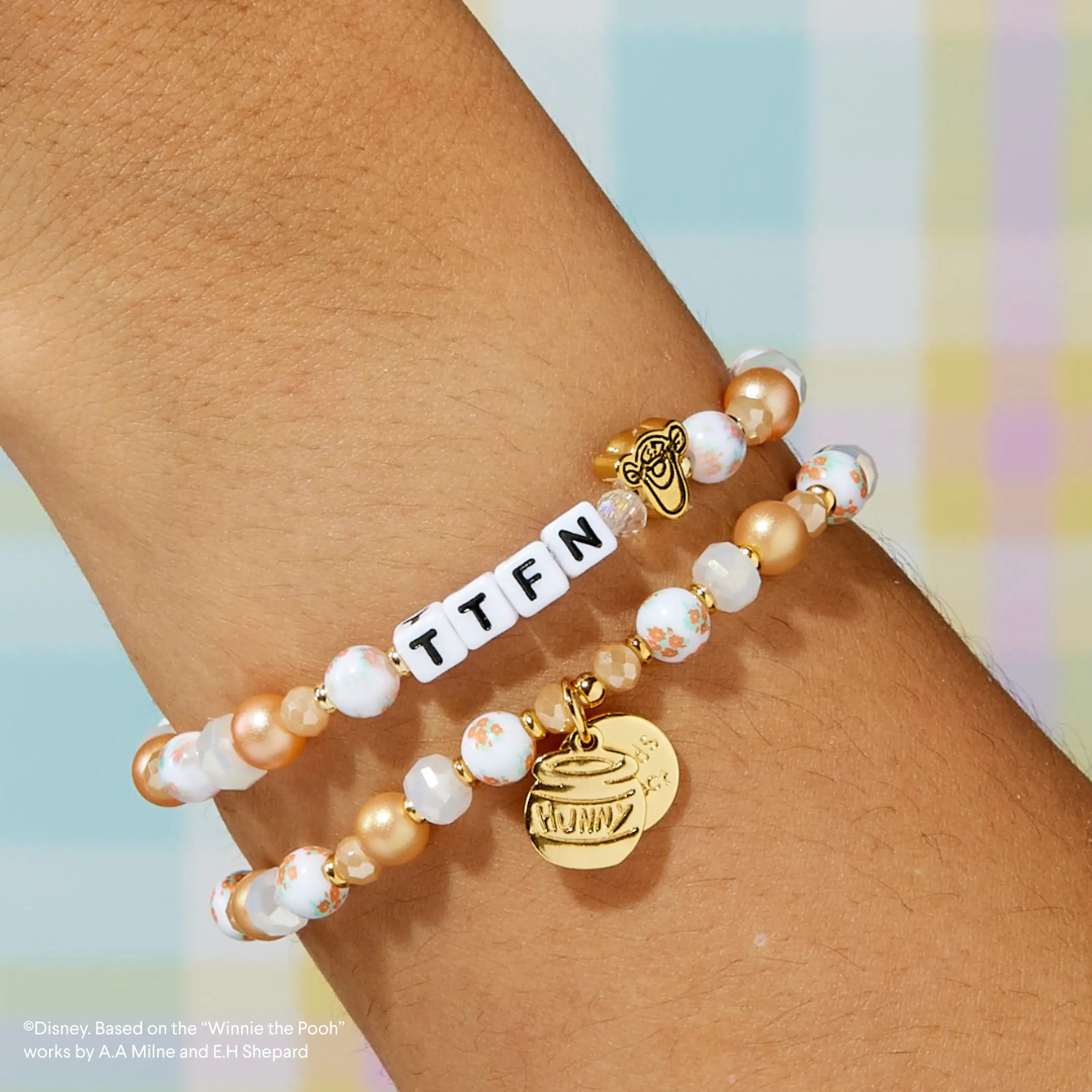 Bracelet with 'TTFN' and a gold tag on a wrist against a colorful background