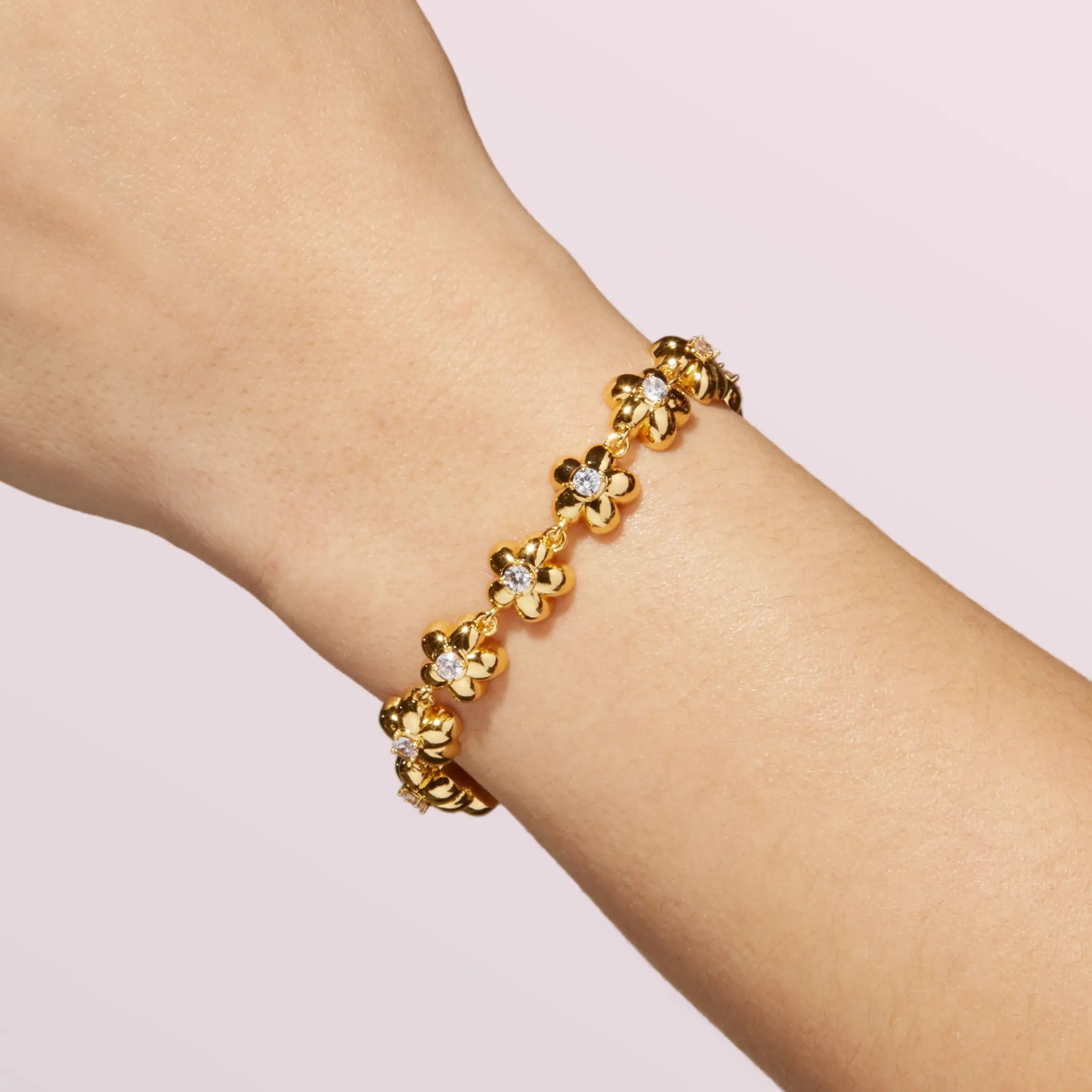 Gold bracelet with floral designs on a wrist against a light pink background