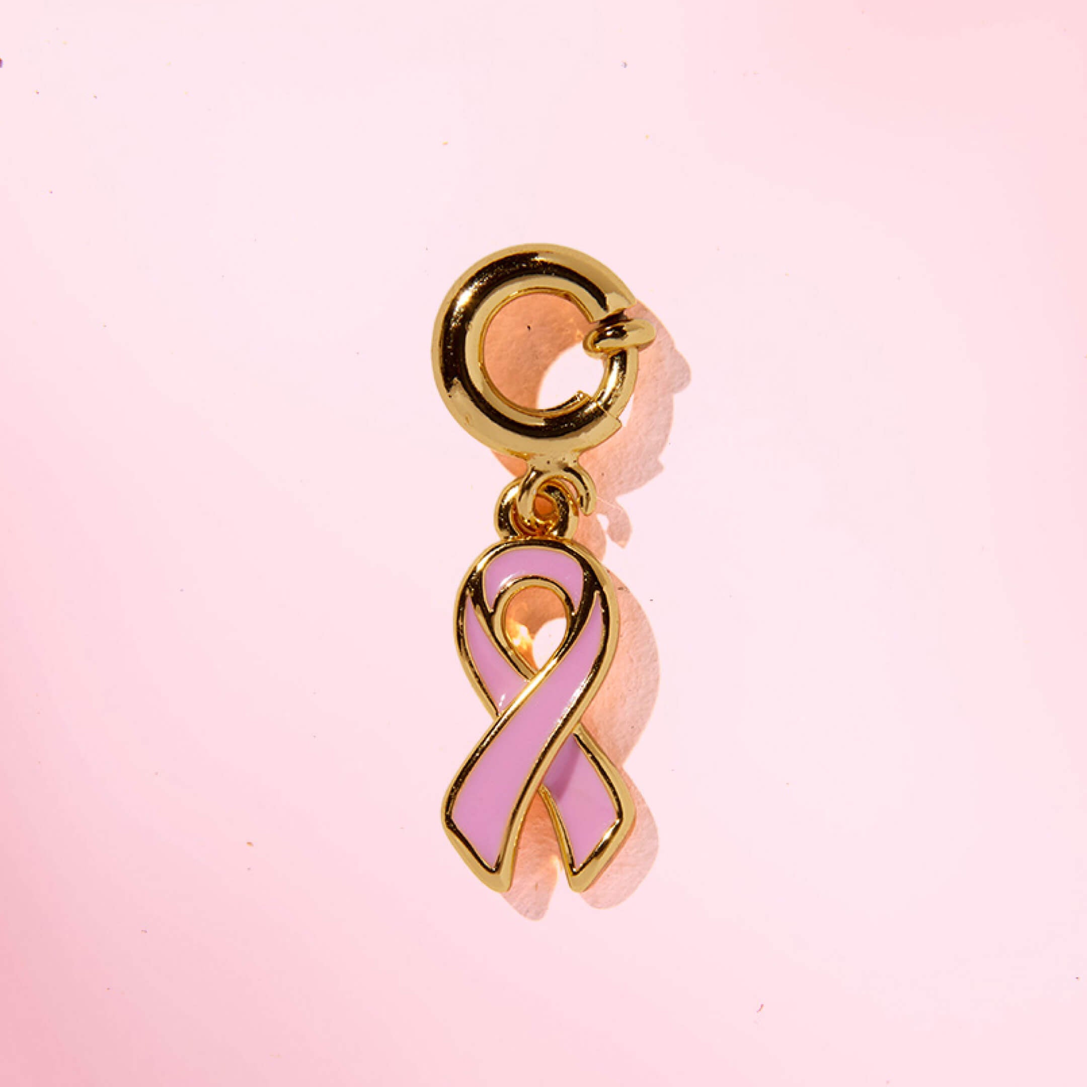 Pink ribbon charm with gold accents on a pink background