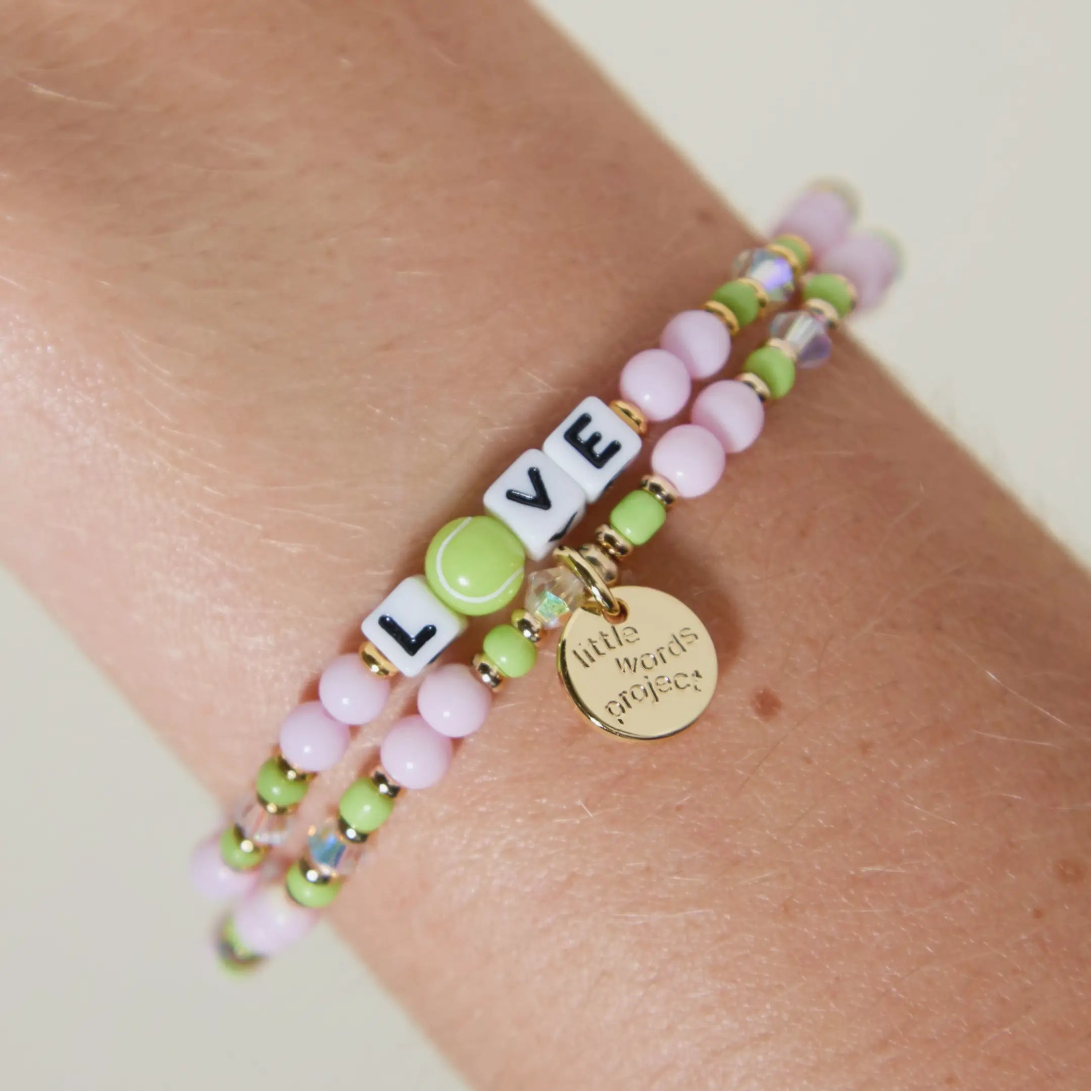 Love tennis bracelet worn on wrist and stacked with a second strand, showing the tennis ball bead O and gold Little Words Project charm
