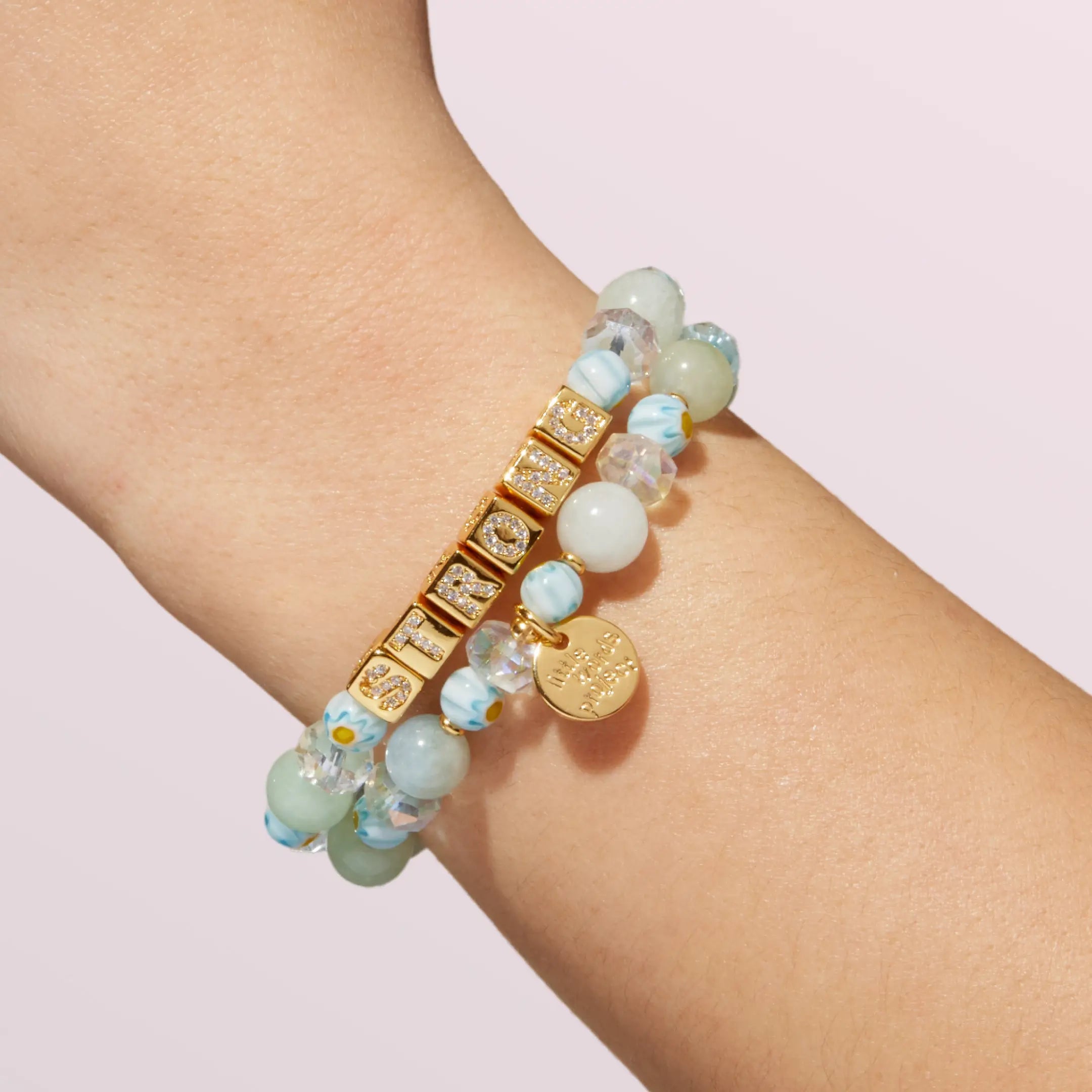 Bracelet with gold accents and light green and blue beads on a wrist against a light background