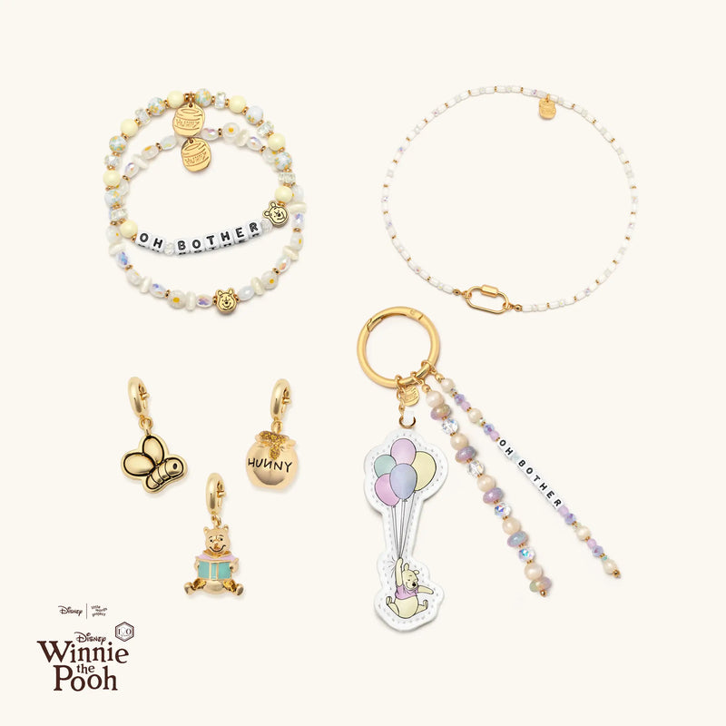 Collection of Winnie the Pooh-themed jewelry and bag charm on a white background with Disney logo.