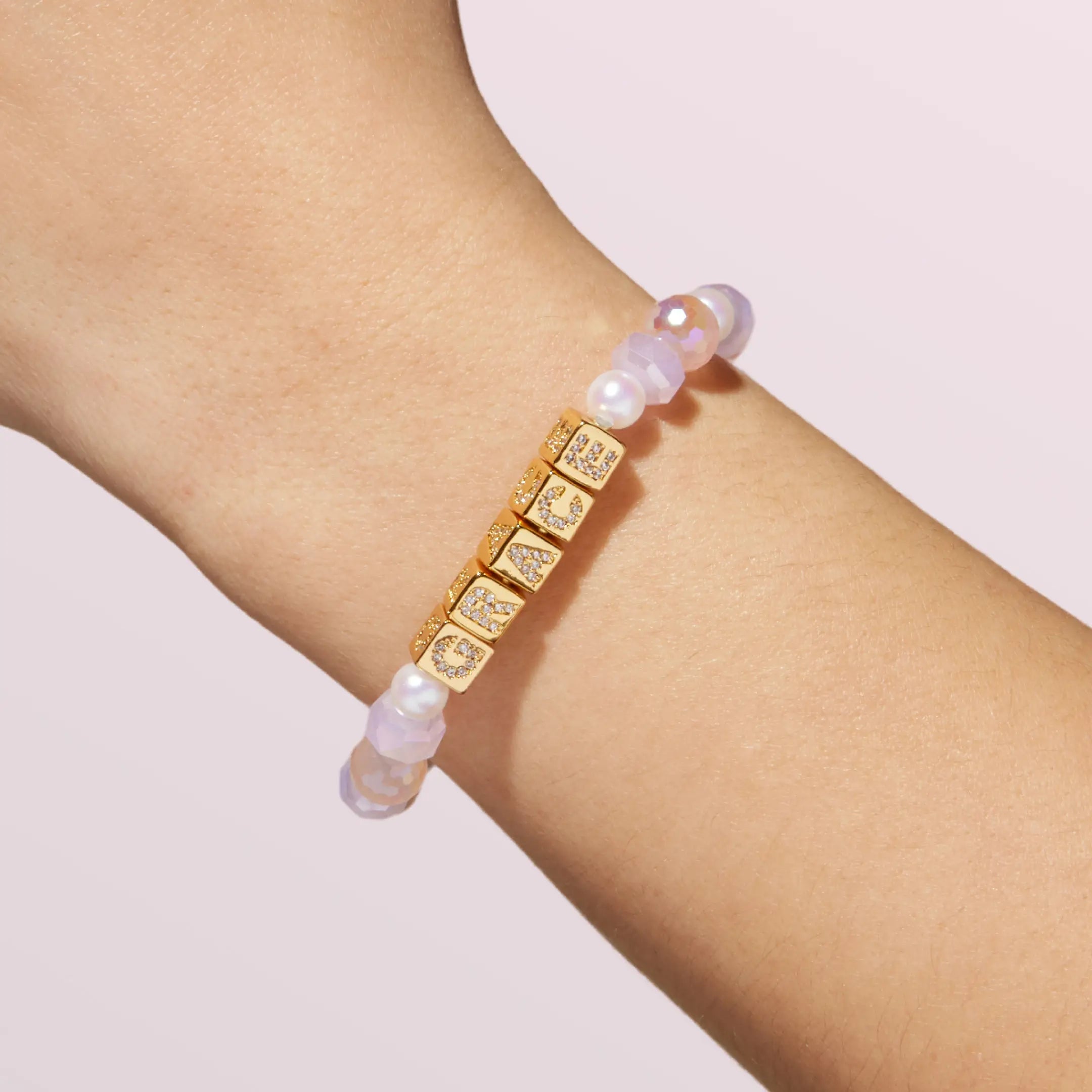 Bracelet with gold square letter beads and pearls on a wrist against a light background