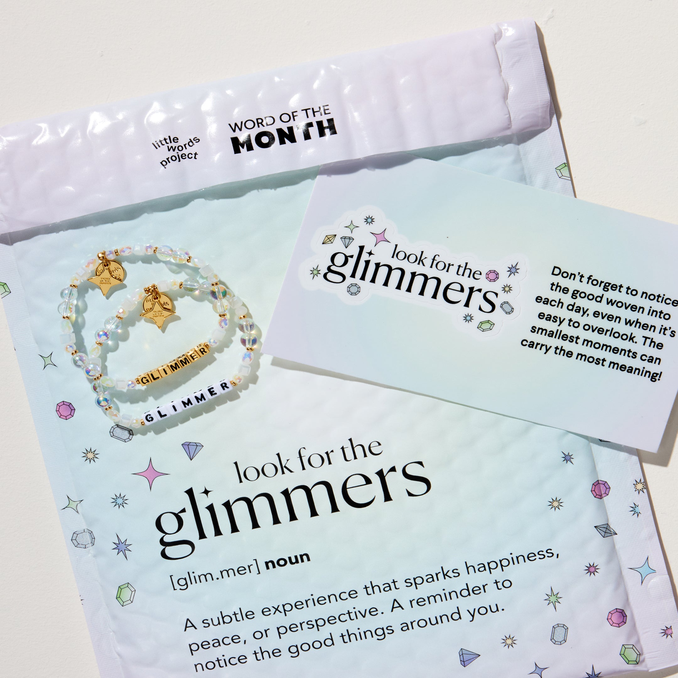 Product packaging for 'look for the glimmers' with an envelope and card on a light background