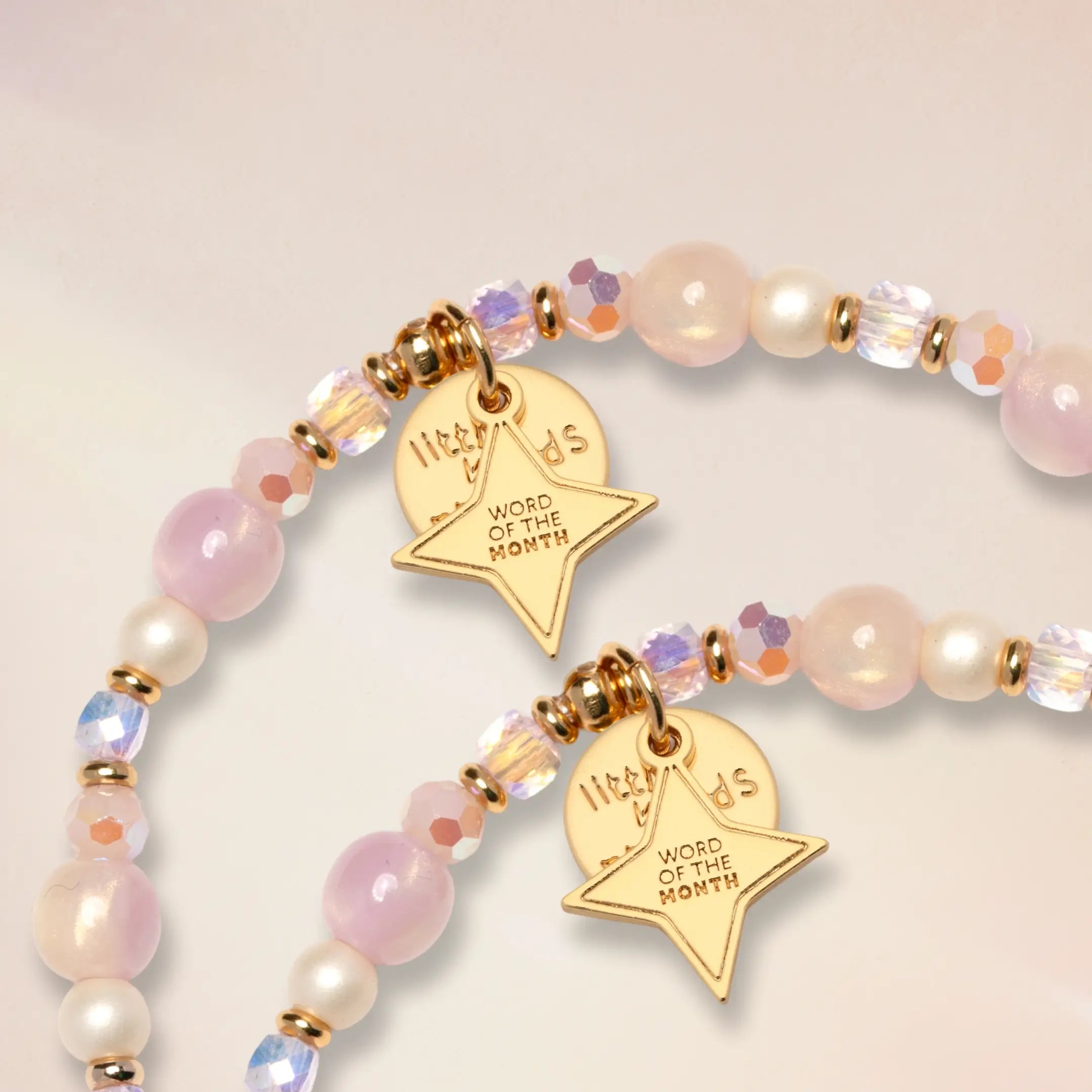 Close-up detail of the gold Little Words Project Word of the Month star charms on two You Are Seen bracelets with pink and cream beads