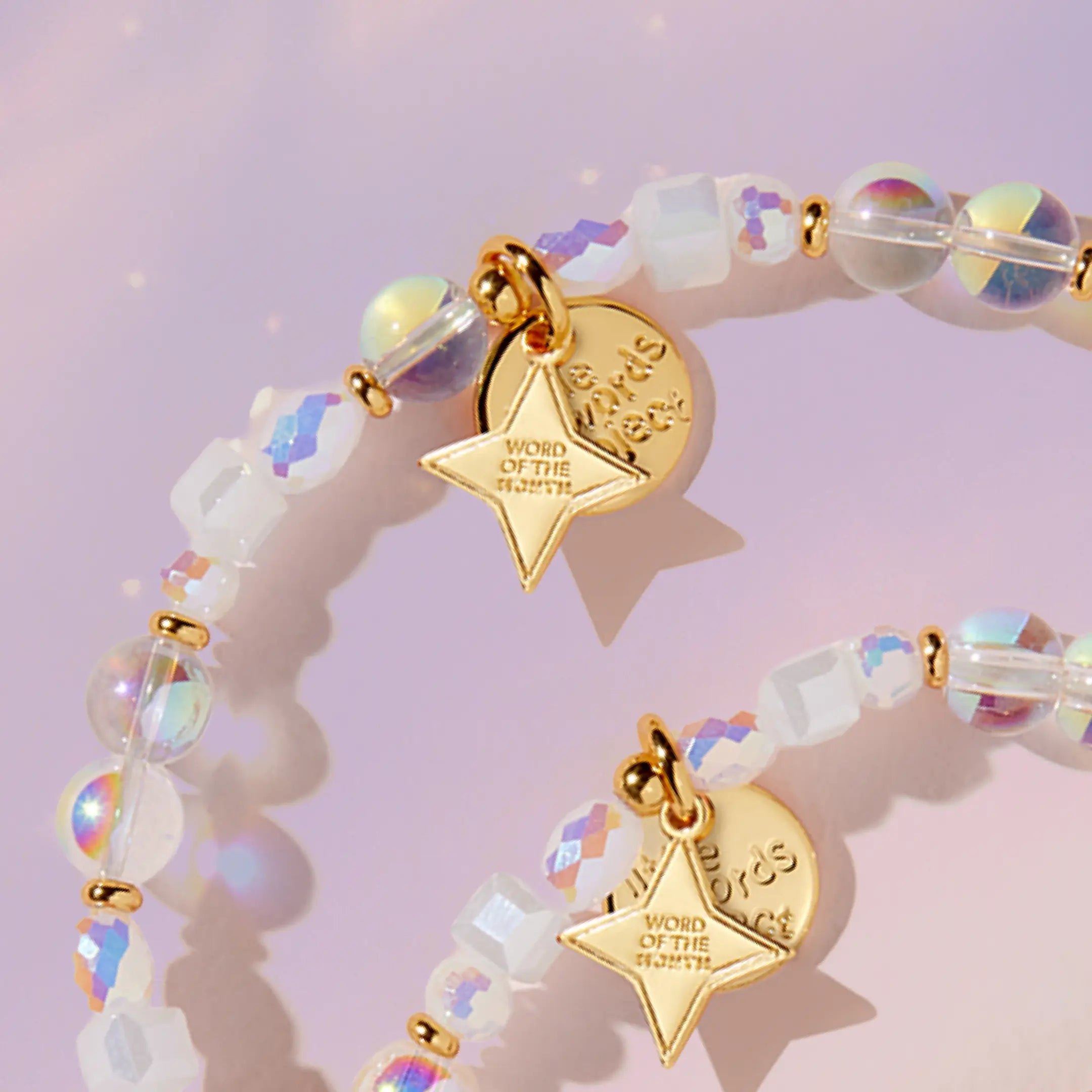 Bracelet with gold charms and iridescent beads on a light pink background
