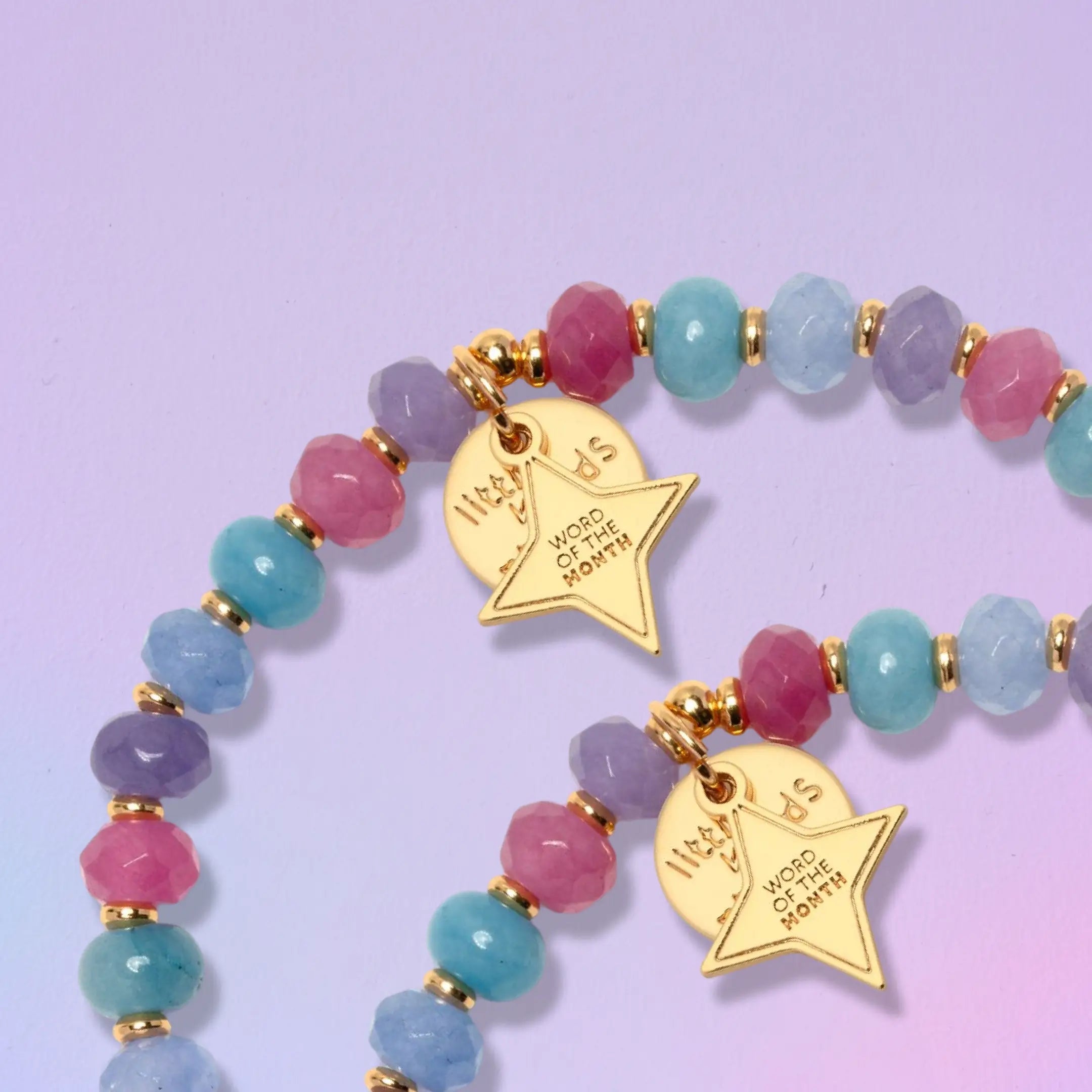 Close up of the gold Word of the Month star charm on two Do Hard Things September bracelets with pink, purple and blue faceted beads