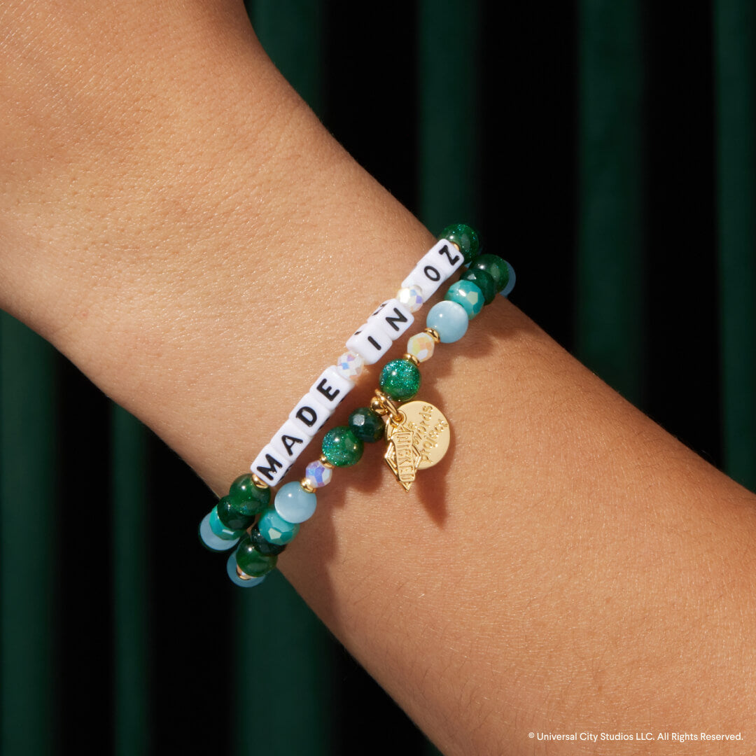 Bracelet with green and blue beads and a gold charm on a wrist against a dark background