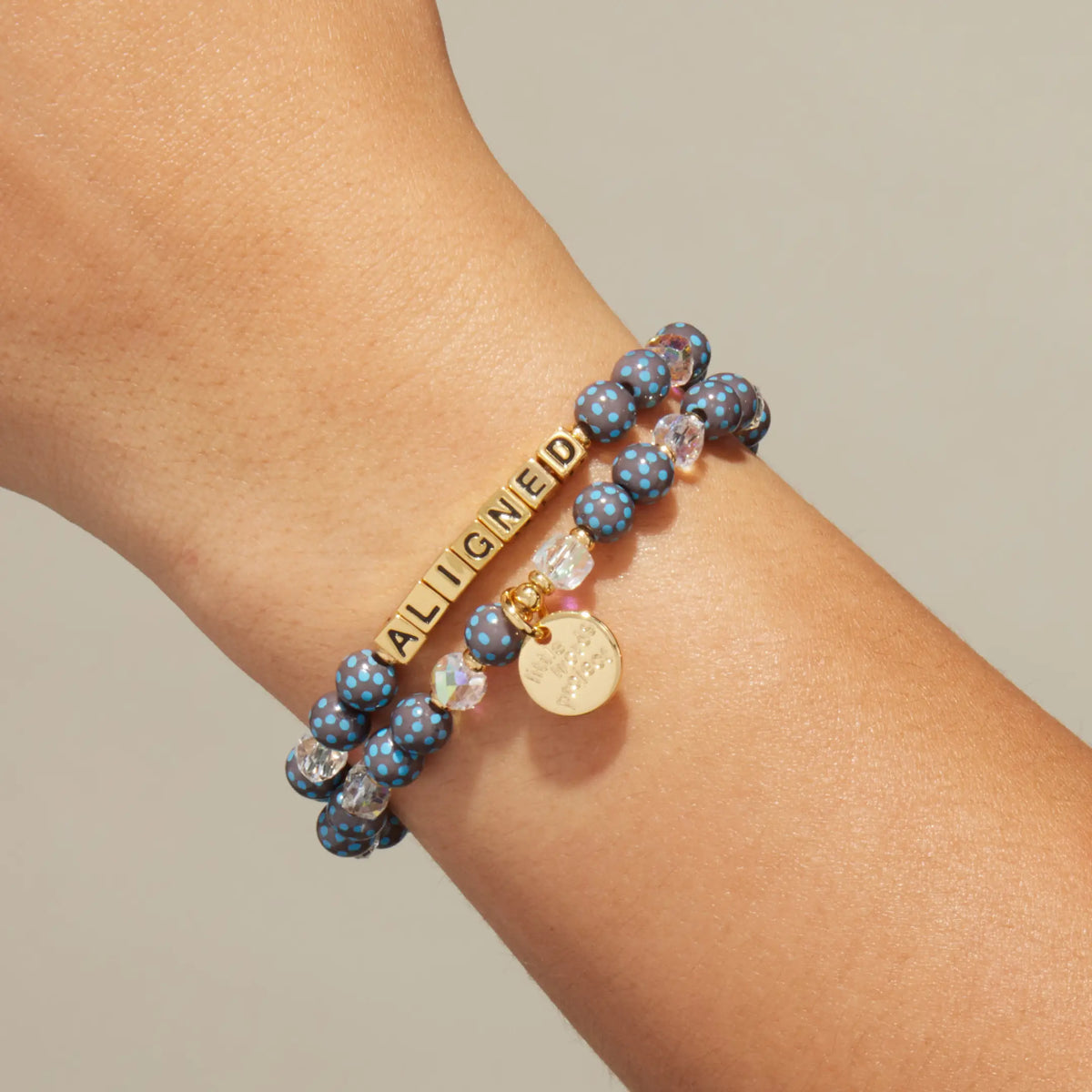 Custom Polky Babe bracelet worn on a wrist, gold letter beads spelling Aligned with dark gray beads with blue polka dots