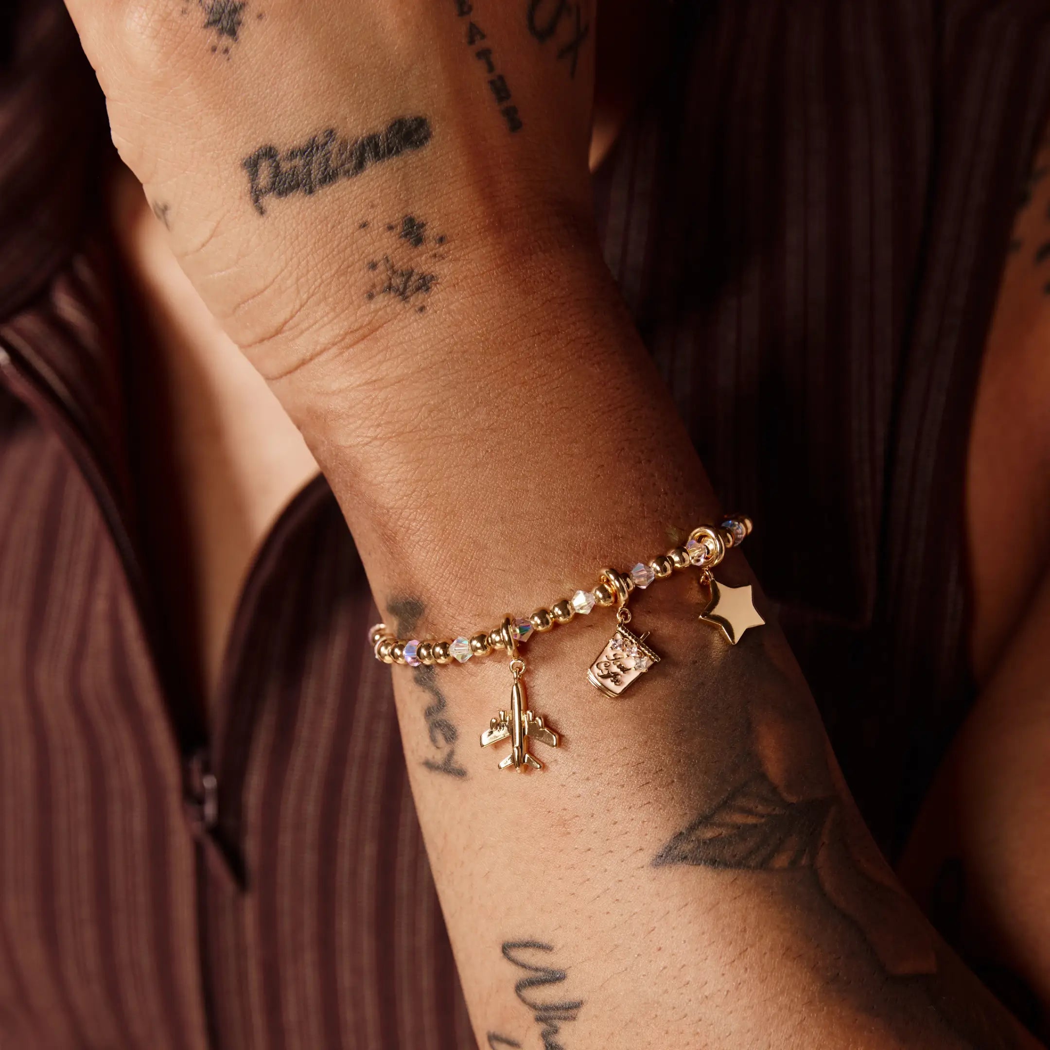Close-up of a wrist with a gold bracelet with charms, set against a dark background.