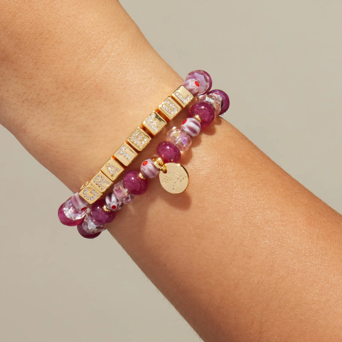 BOLDER Custom Rosemary bracelet worn on a wrist, gold CZ letter blocks spelling Grateful with raspberry jade and plum floral glass beads