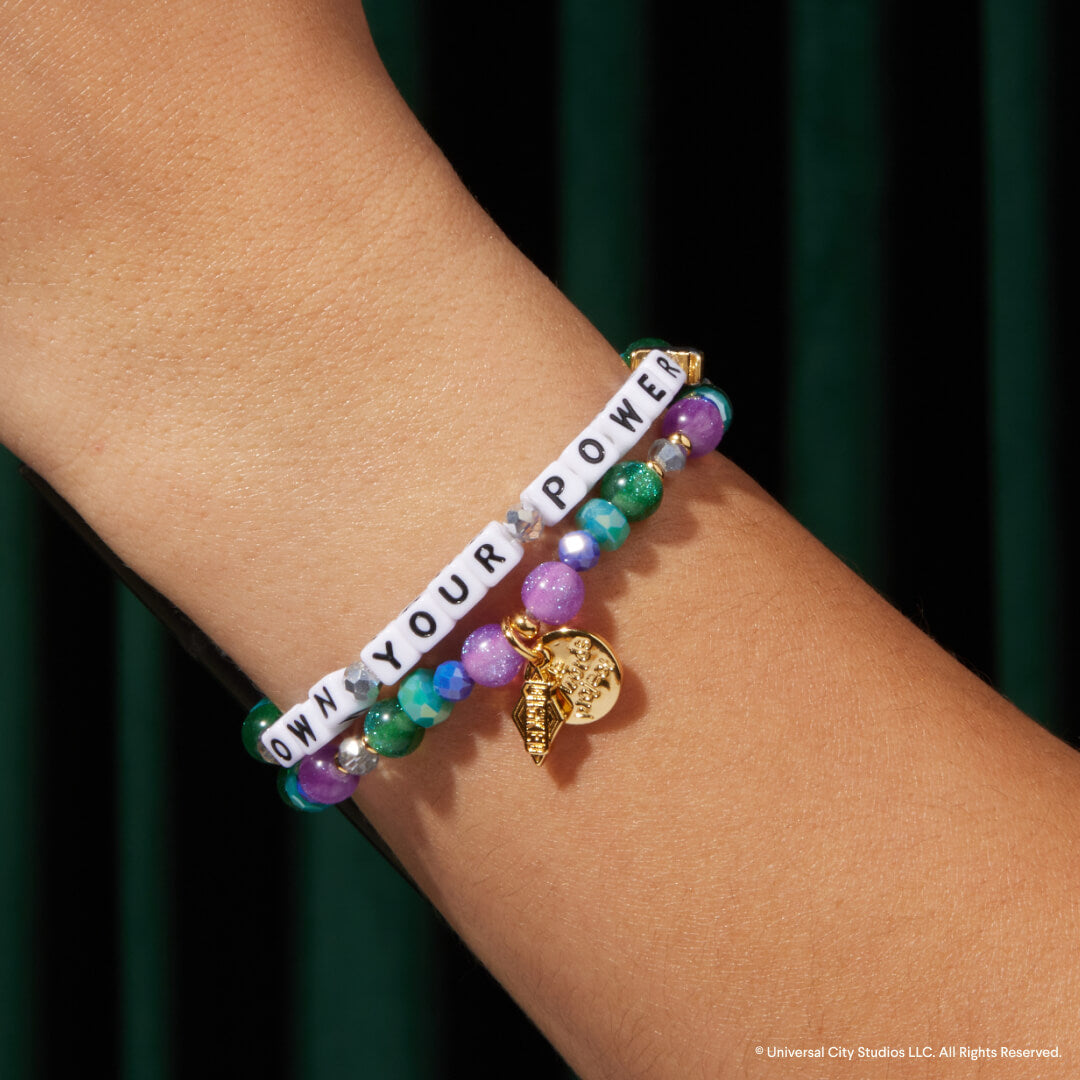 Multicolored beaded bracelet with gold charm on wrist against a dark green background