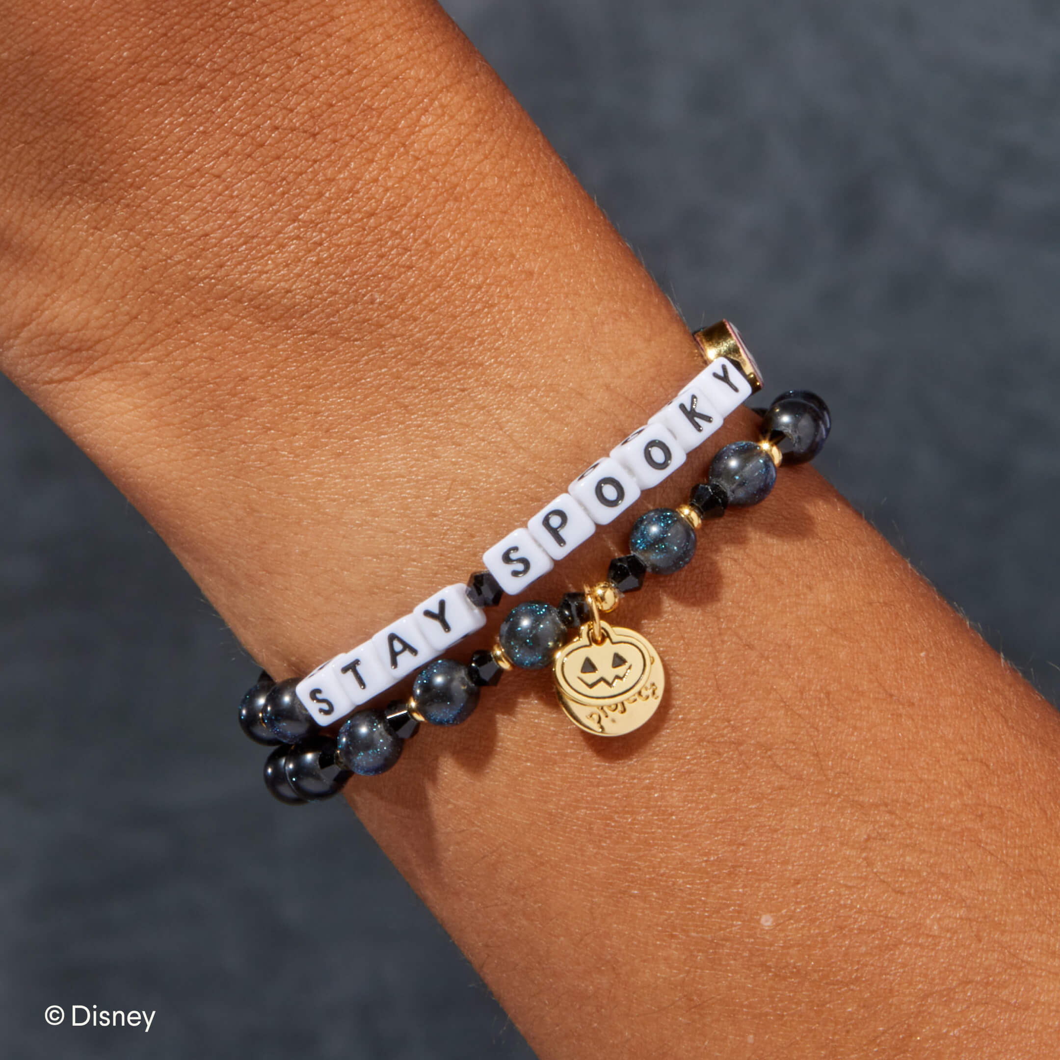 Bracelet with 'STAY SPOOKY' text and pumpkin charm on a wrist against a dark background