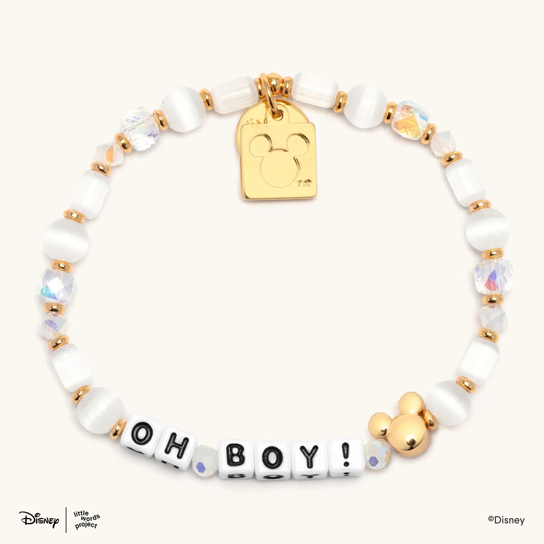 Oh Boy! Disney Mickey and Friends bracelet flat lay on cream with white beads, black and white letter beads, a gold Mickey Mouse bead and a gold plated casted Mickey Mouse tag charm