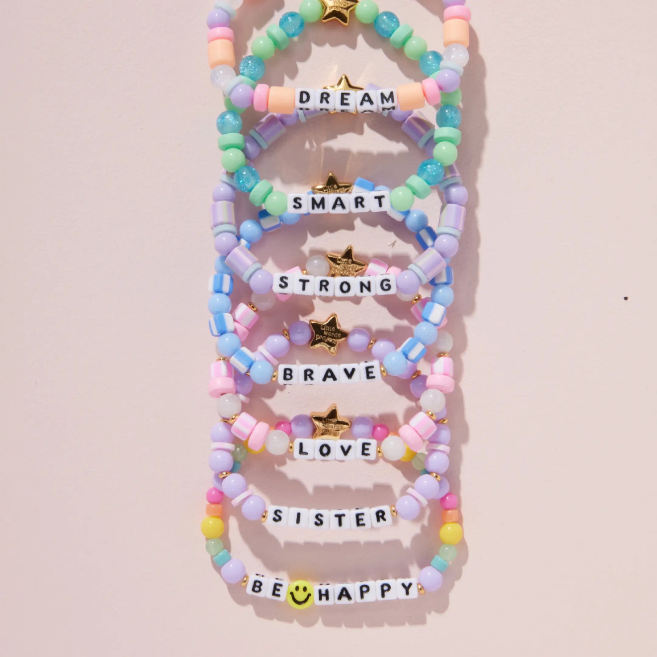 Colorful beaded bracelets with motivational phrases on a light pink background