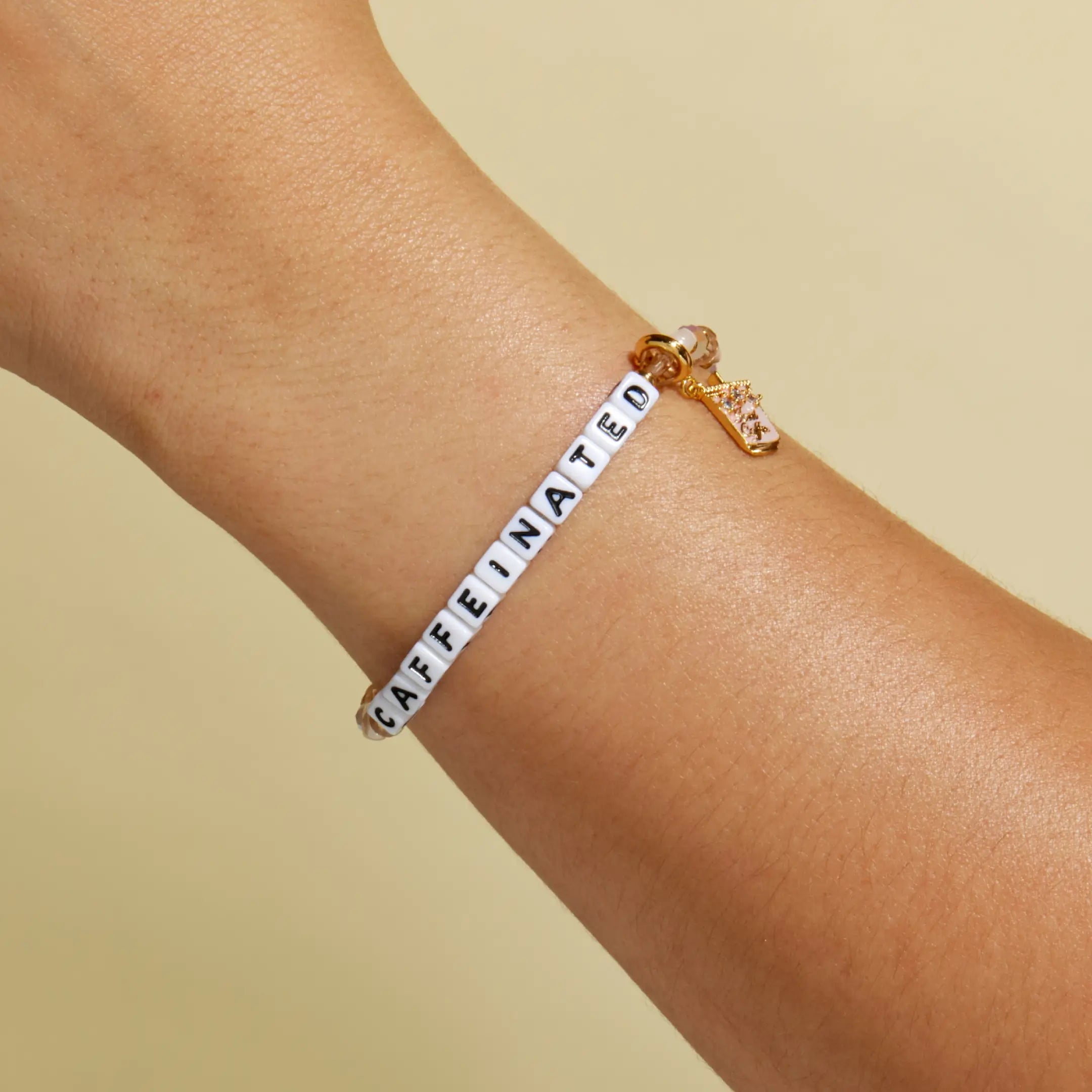Bracelet with 'CAFFEINATED' on a wrist against a beige background