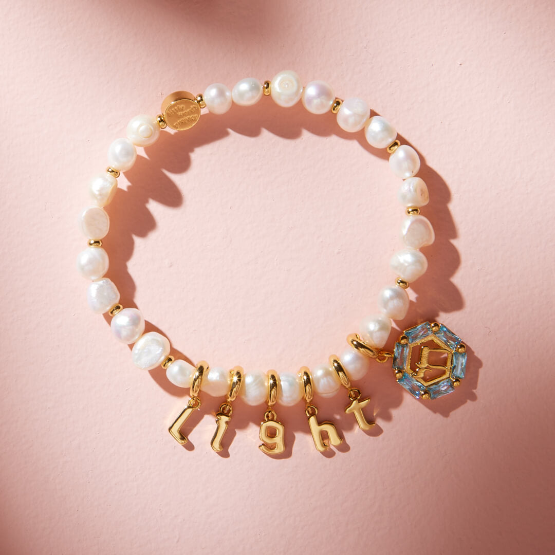 Pearl bracelet with gold charms on a pink background
