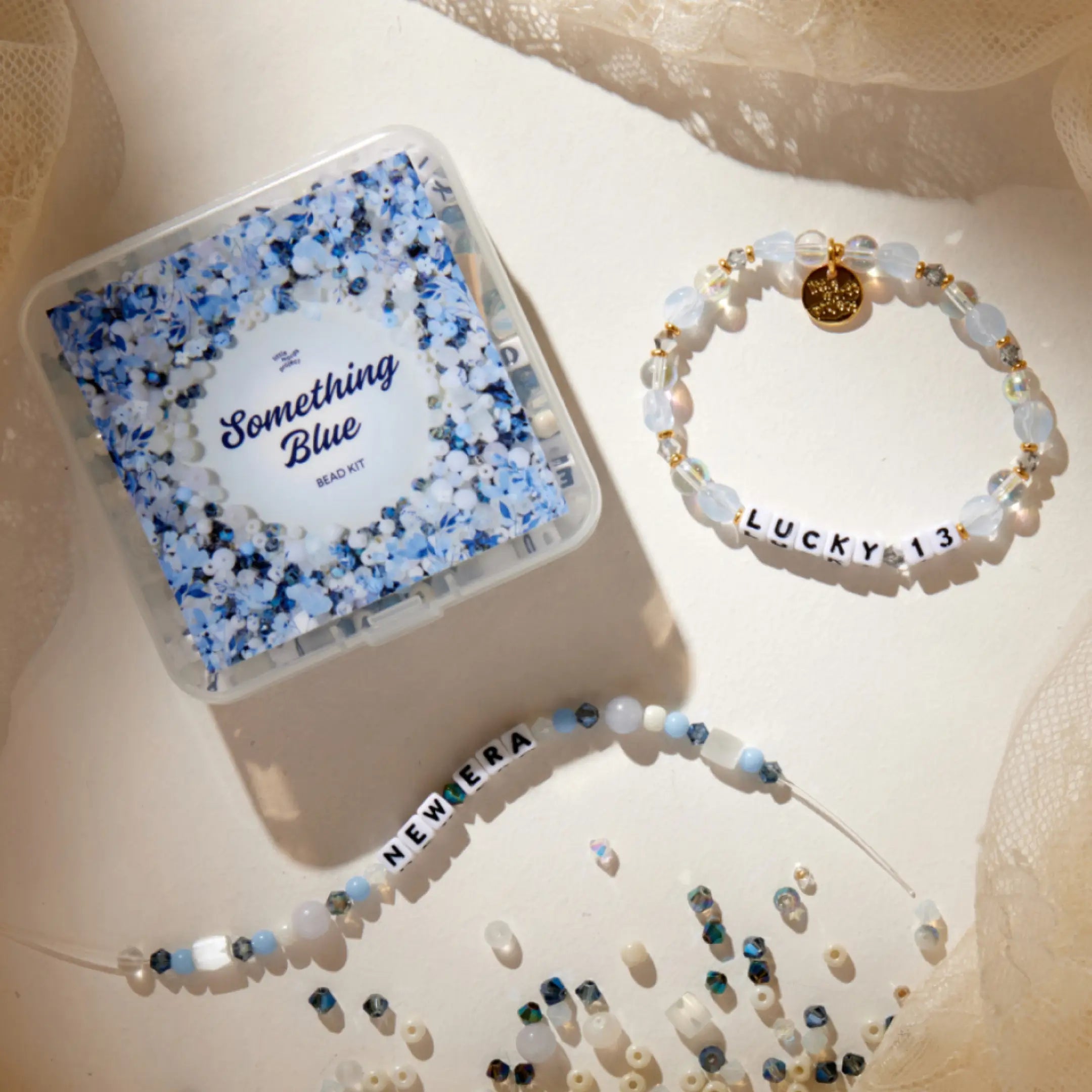 Something Blue bead kit box on lace beside finished and in-progress bracelets made from the kit, with loose blue and white beads scattered around