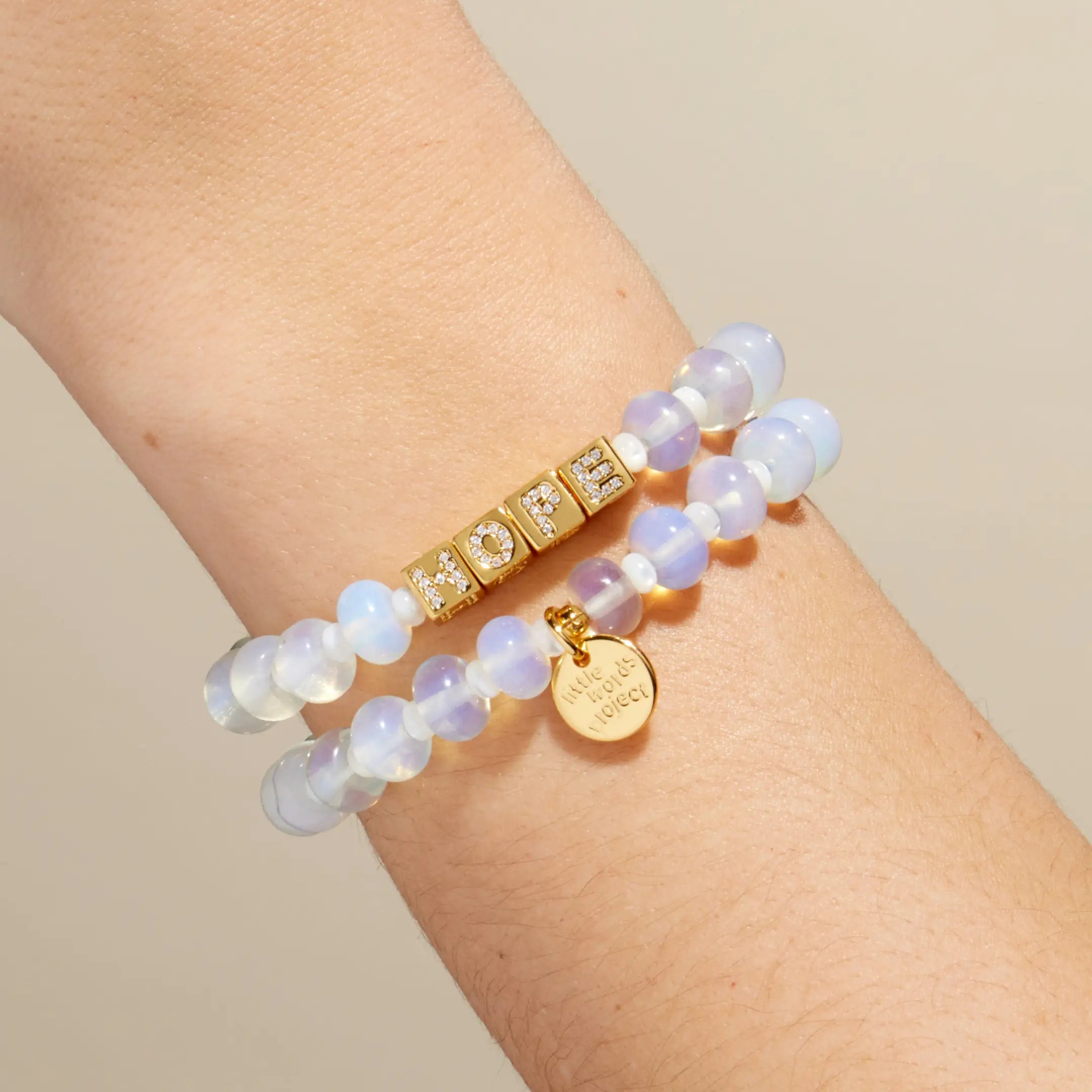 Two bracelets on a wrist against a beige background