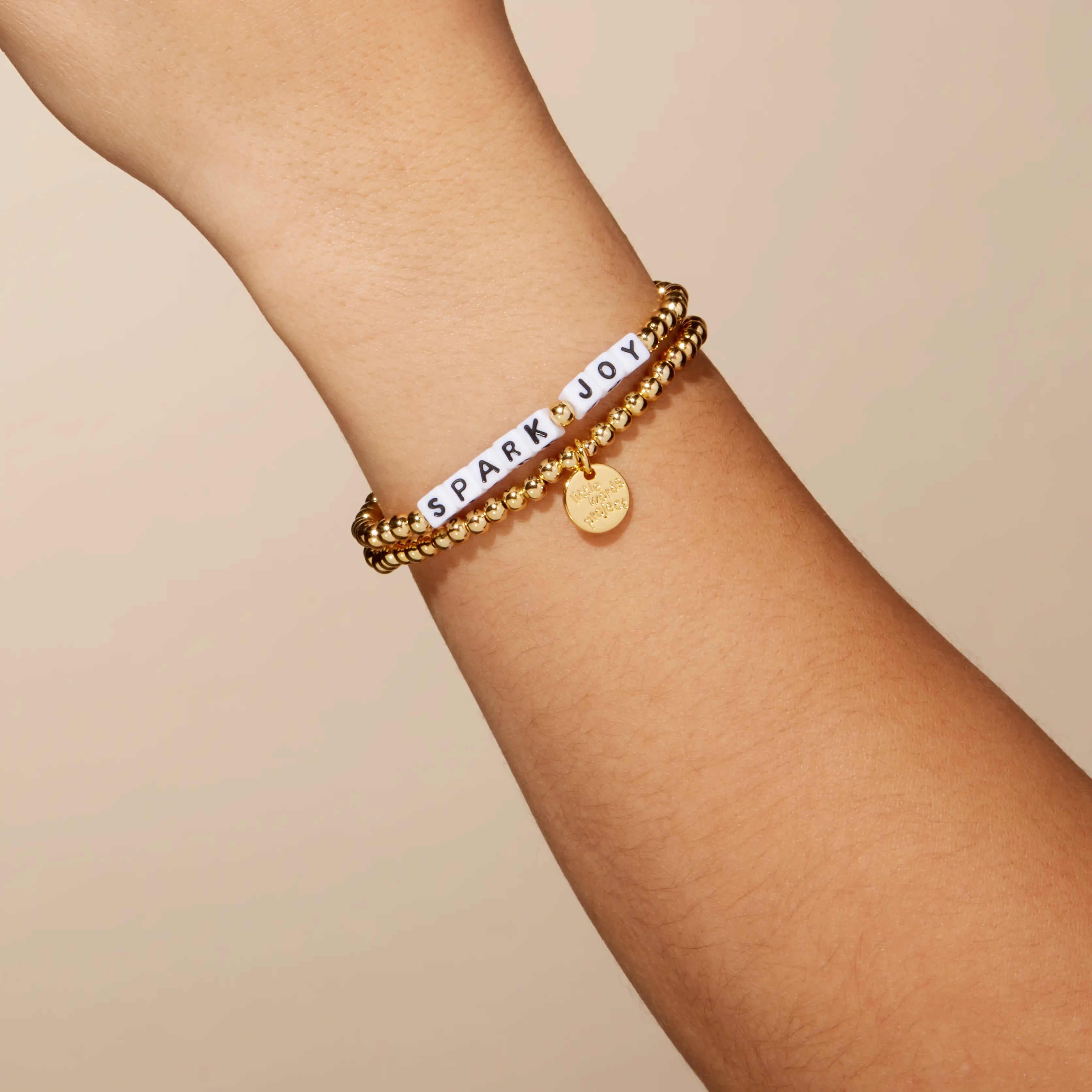 Gold bracelet with  text on a wrist against a beige background
