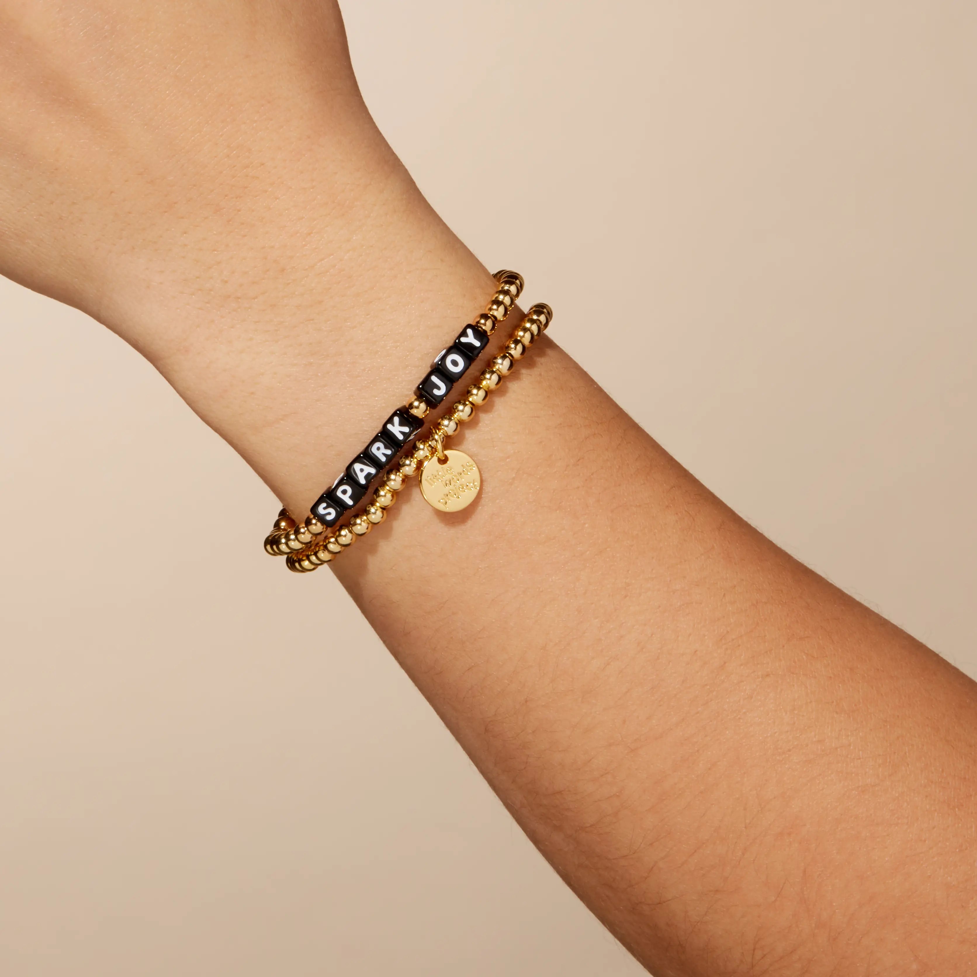 Gold bracelet with text on a wrist against a beige background