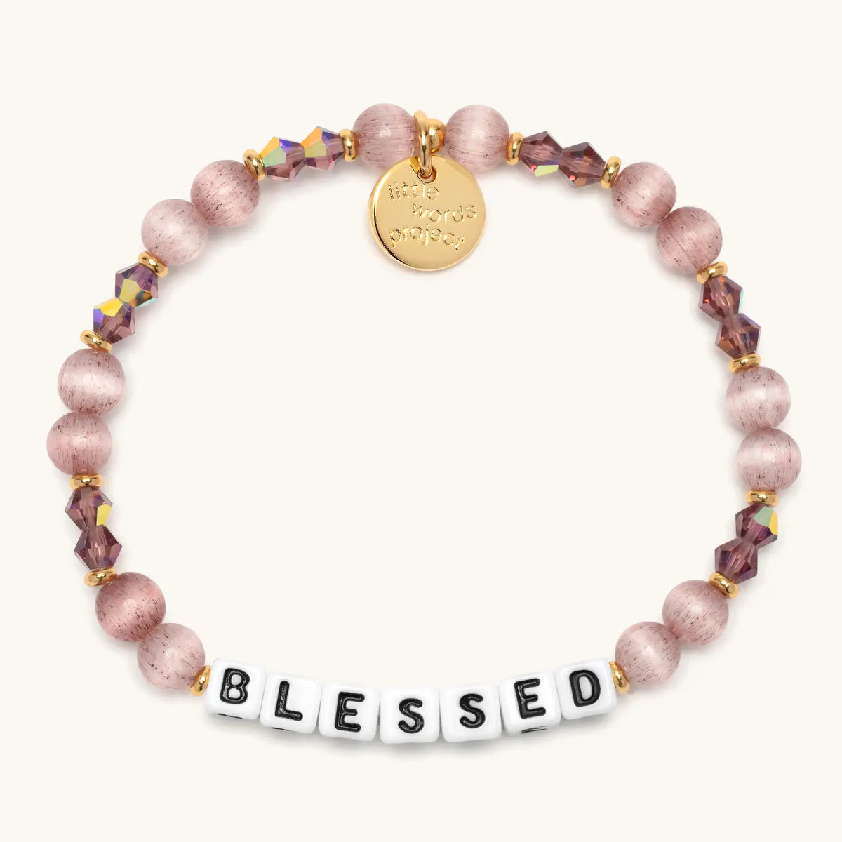 Blessed bracelet in the Holiday Spritz bead pattern, white letter beads with mauve cat's eye beads and faceted purple crystals with gold accents, flat-lay on cream background