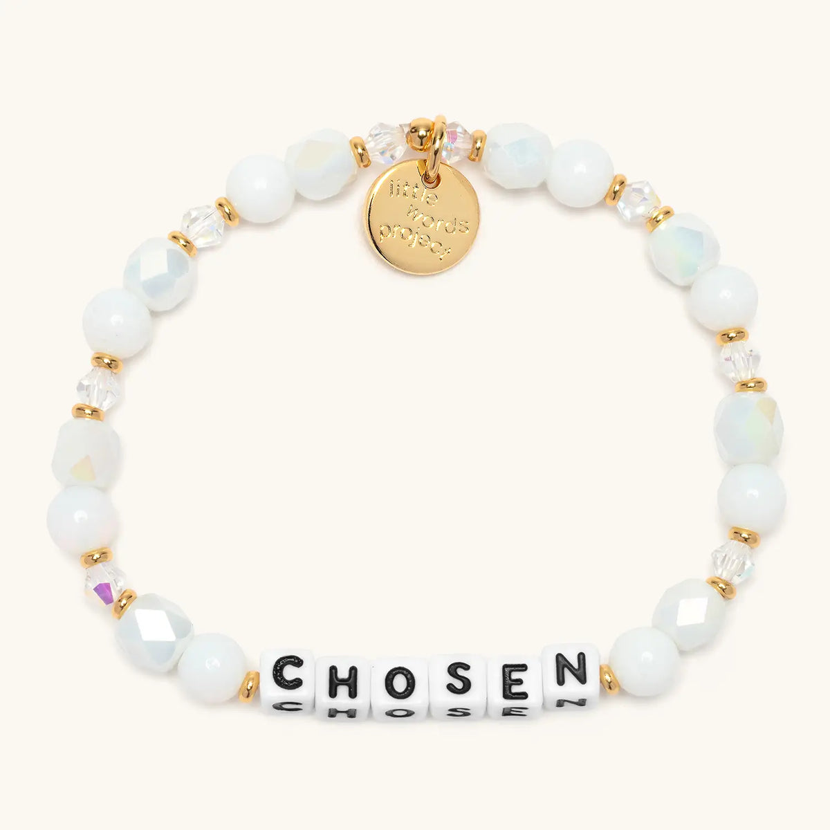 Chosen bracelet in the Snow Fantasy bead pattern, white letter beads with white glass beads, iridescent white faceted beads, and clear crystals with gold accents, flat-lay on cream background