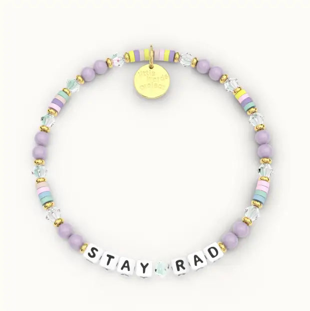 A pastel beaded bracelet with lavender, mint, pink, and yellow beads, gold spacer beads, a round gold charm, and white letter beads spelling 'STAY RAD' on a light off-white background.