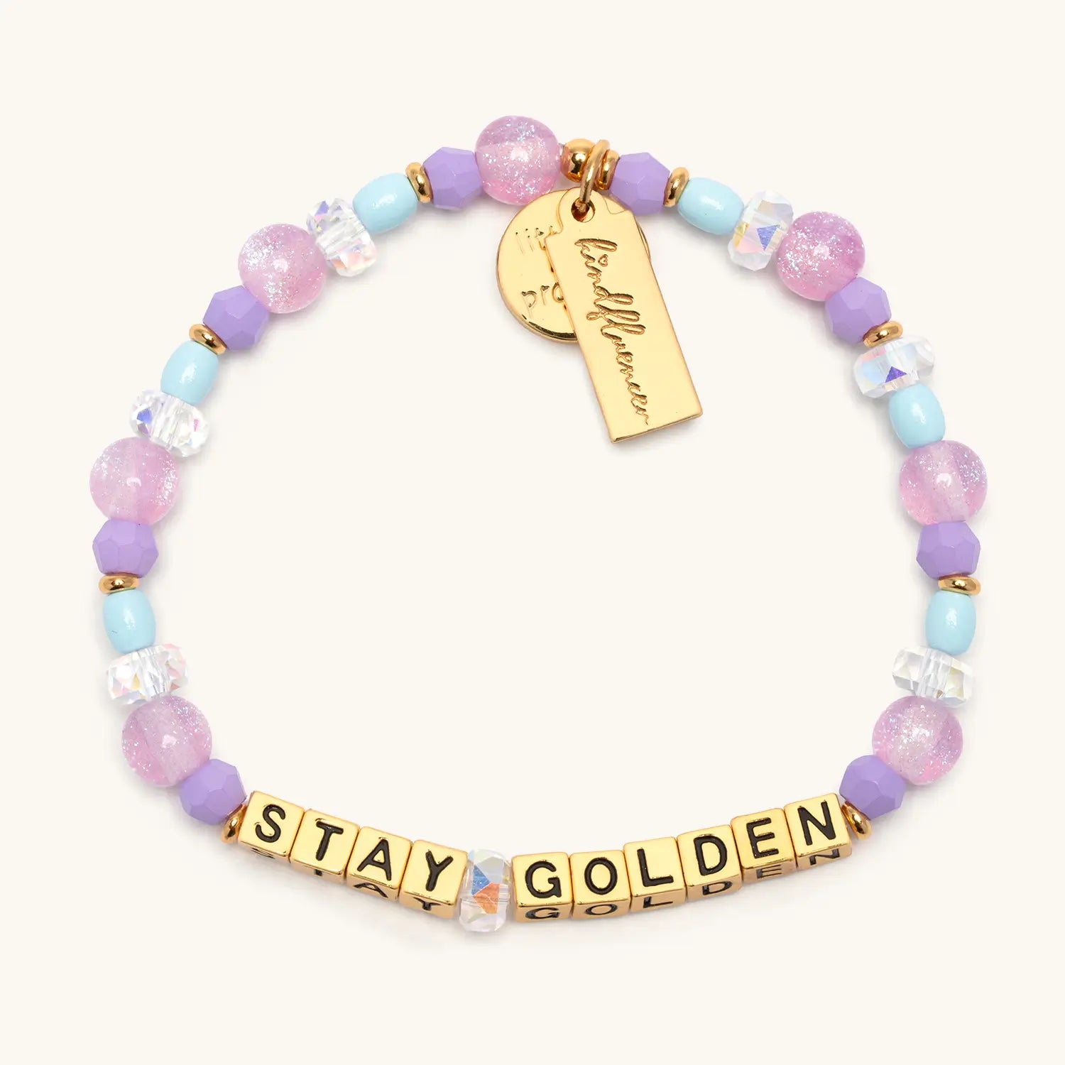Stay Golden Rylee Ta bracelet with gold letter beads, lavender and pink crystal beads, light blue and cream beads, gold star charm and Little Words Project tag, flat lay on cream background