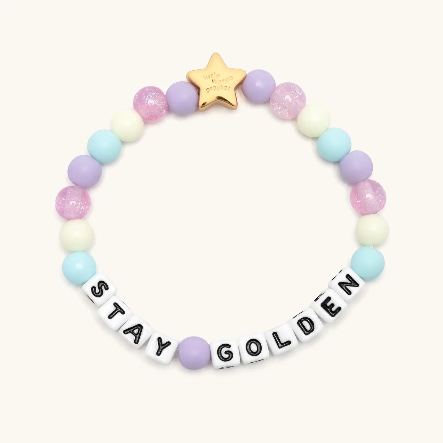 Stay Golden Kids Rylee Ta bracelet in size XXS with white letter beads, purple, light blue and cream beads and a gold star charm, flat lay on cream background