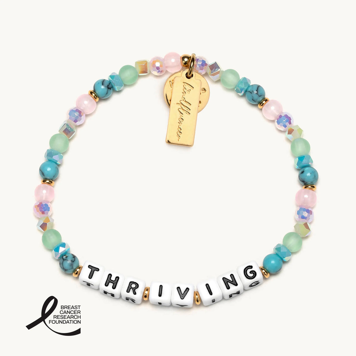 Thriving bracelet by Katie Thurston, white letter beads with turquoise stone, pink, sea green frosted glass, and iridescent crystal beads with gold accents and a gold Kindfluencer tag, flat-lay on cream background with the Breast Cancer Research Foundation logo