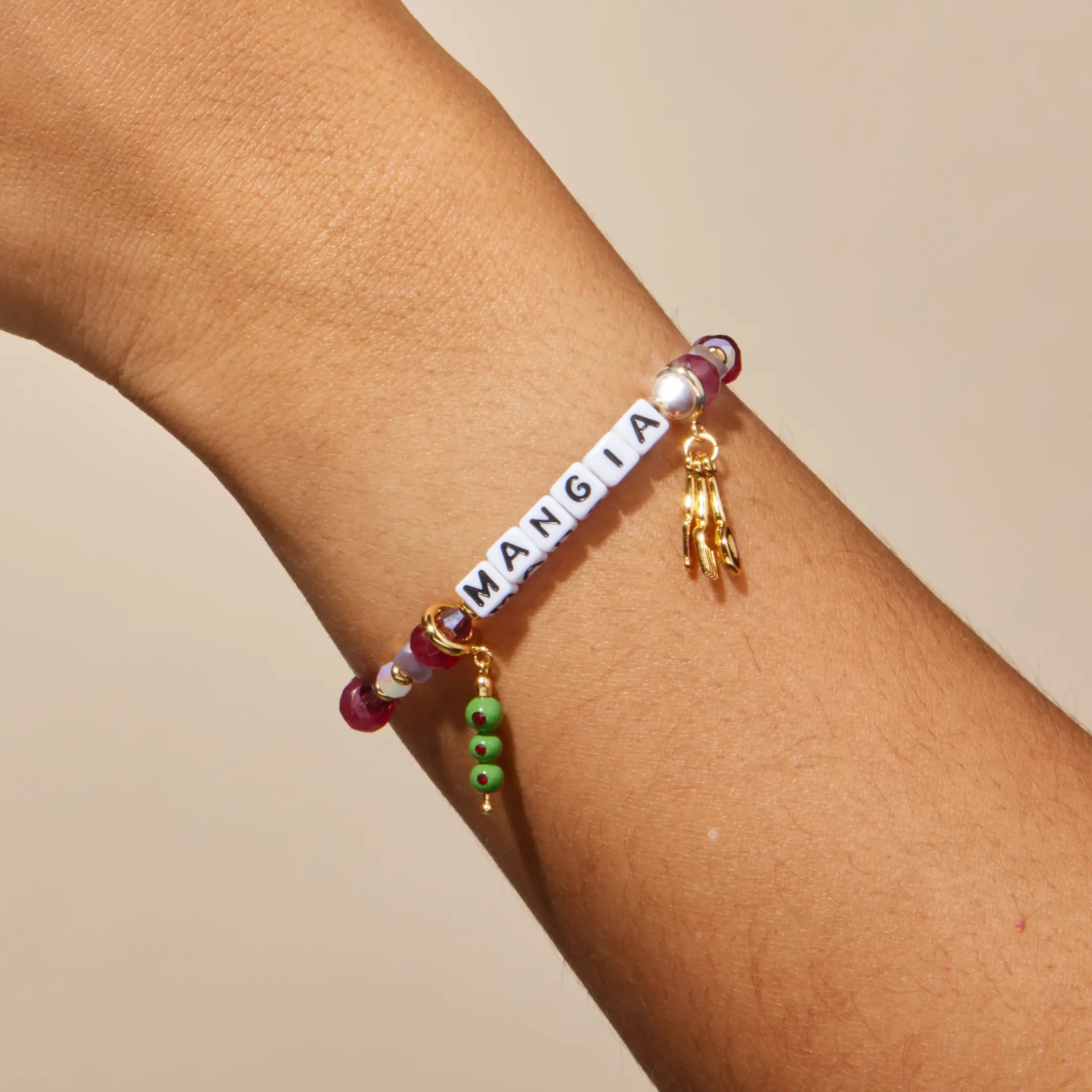 Bracelet with colorful beads and a gold charms on a wrist against a beige background