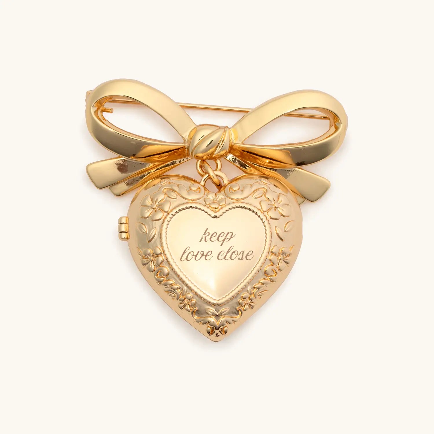 Gold heart-shaped locket with 'keep love close' engraving and bow on a white background