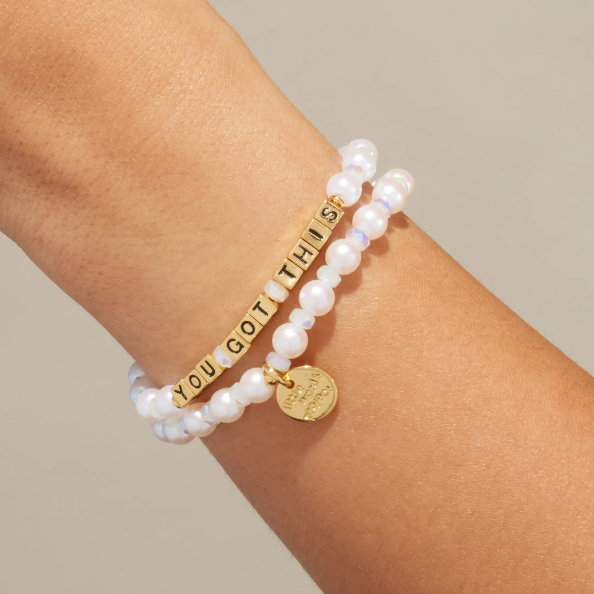 Gold You Got This bracelet in the Cloud Crush bead pattern with gold letter beads, stacked with a coordinating beaded bracelet, on-model on wrist against cream background