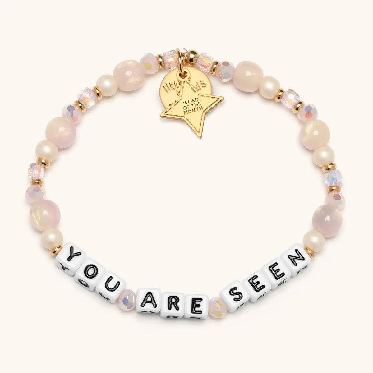 You Are Seen August Word of the Month bracelet with white letter beads spelling YOU ARE SEEN, strung with cream, blush, taupe and soft gray beads, shown flat lay in a circle on a white background