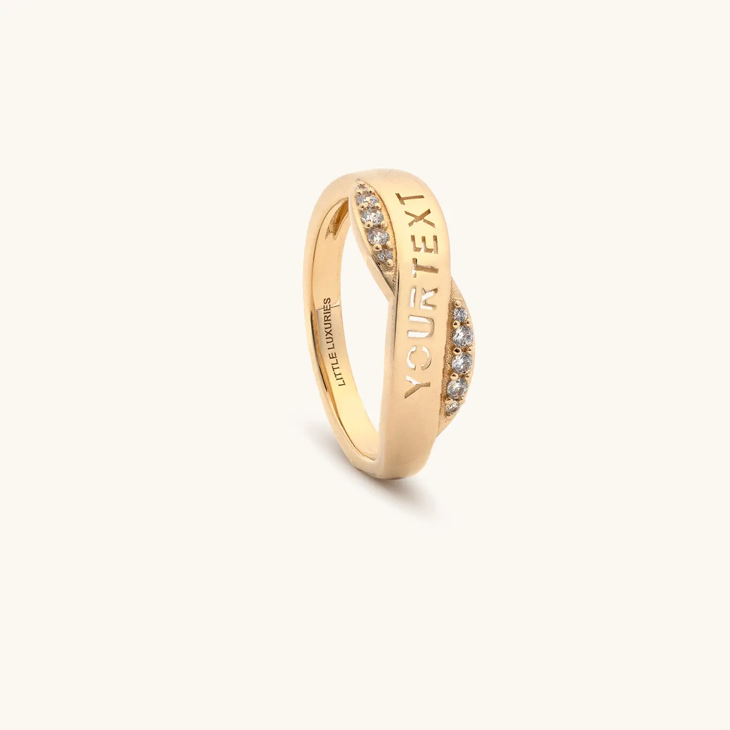 A custom gold ring with a twisted band design, featuring small clear pavé-set stones on the sides and the customizable text 'YOURTEXT' engraved on one side. 